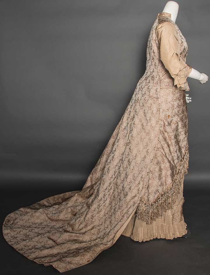SILK BROCADE RECEPTION DRESS, 1875-1885: 1-piece abstract geometric pattern in taupe, brown, & tan silk faille, boned bodice attaches to skirt at CB, sleeves & CF skirt panel of tan silk faille, long trained skirt edged in multi-colored silk