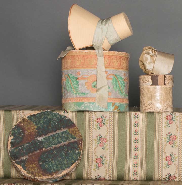 TWO DOLL BONNETS & WALLPAPER BOXES, 1830-1840: 1 tan silk Quaker bonnet & brown print box, HT 3", bonnet excellent, box very good; 1 faux straw paper bonnet, straw braid & blue ribbon trims, peach, gray & green box, HT 6", (breaks in braid & lid d
