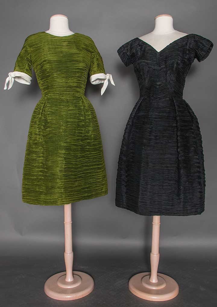 TWO SYBIL CONNOLLY PARTY DRESSES, 1960s: Both labeled & fabric horizontally hand pleated: 1 black silk, V F&B neckline, short cap sleeves & pleated bell skirt, B 36", W 27", L 42.5"; 1 olive green short sleeve w/ narrow white trim, bell skir