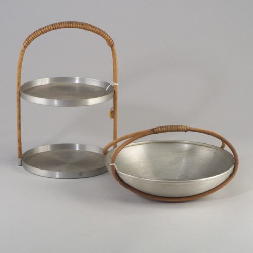 Two RUSSEL WRIGHT spun aluminum pieces: Two RUSSEL WRIGHT spun aluminum pieces: a two-tiered stand and a fruit basket, both with rattan and cane handles. Some light scratches, also small ding to exterior of fruit basket. Stand stamped "Russ