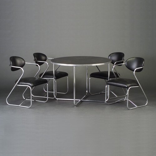GILBERT ROHDE: TROY SUNSHADE circular table with black top and bright chrome tubular legs and trim, together with four bright chrome tubular chairs upholstered in black vinyl. Troy Sunshade decals. Table: 29" x 42"