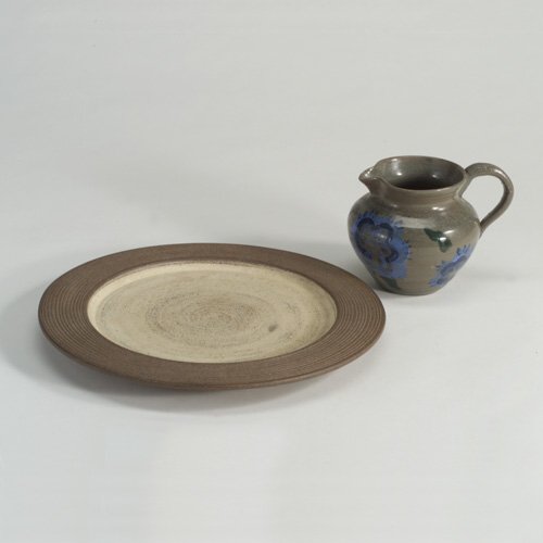 SCHEIER: Two stoneware pieces: small pitcher by MARY SCHEIER decorated with blue flowers and green leaves on a gray ground; and a plate in brown and cream. Both marked. 4 3/4" h and 12" dia.