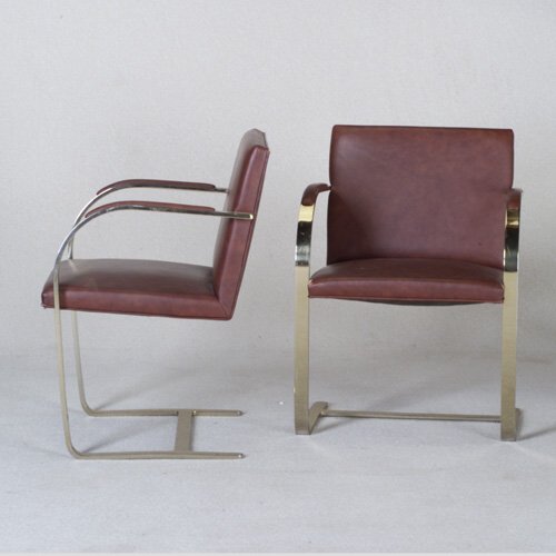 BRUETON: Pair of Brno-style armchairs with reddish-brown upholstery to seat, back, and armrests, on cantilevered flat steel base. Paper label. 31" x 23" x 20"