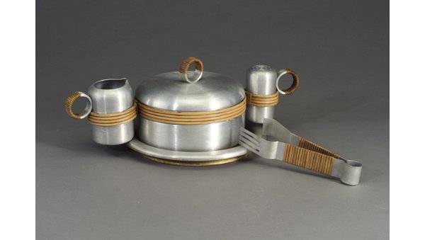 Five-piece RUSSEL WRIGHT spun aluminum a: Five-piece RUSSEL WRIGHT spun aluminum and wrapped willow spaghetti service consisting of a covered serving bowl with holder for cheese shaker and sauce pitcher, tongs, and circular tray with wood sur
