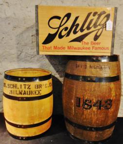 Wood Barrels and Beer Crates: This group includes a wood Schlitz Brewing Company barrel, a wood Schlitz 2 dozen bottle case with metal seaming and handles, and an oak barrel with 1843 printed on it. The beer case has the Schlitz g