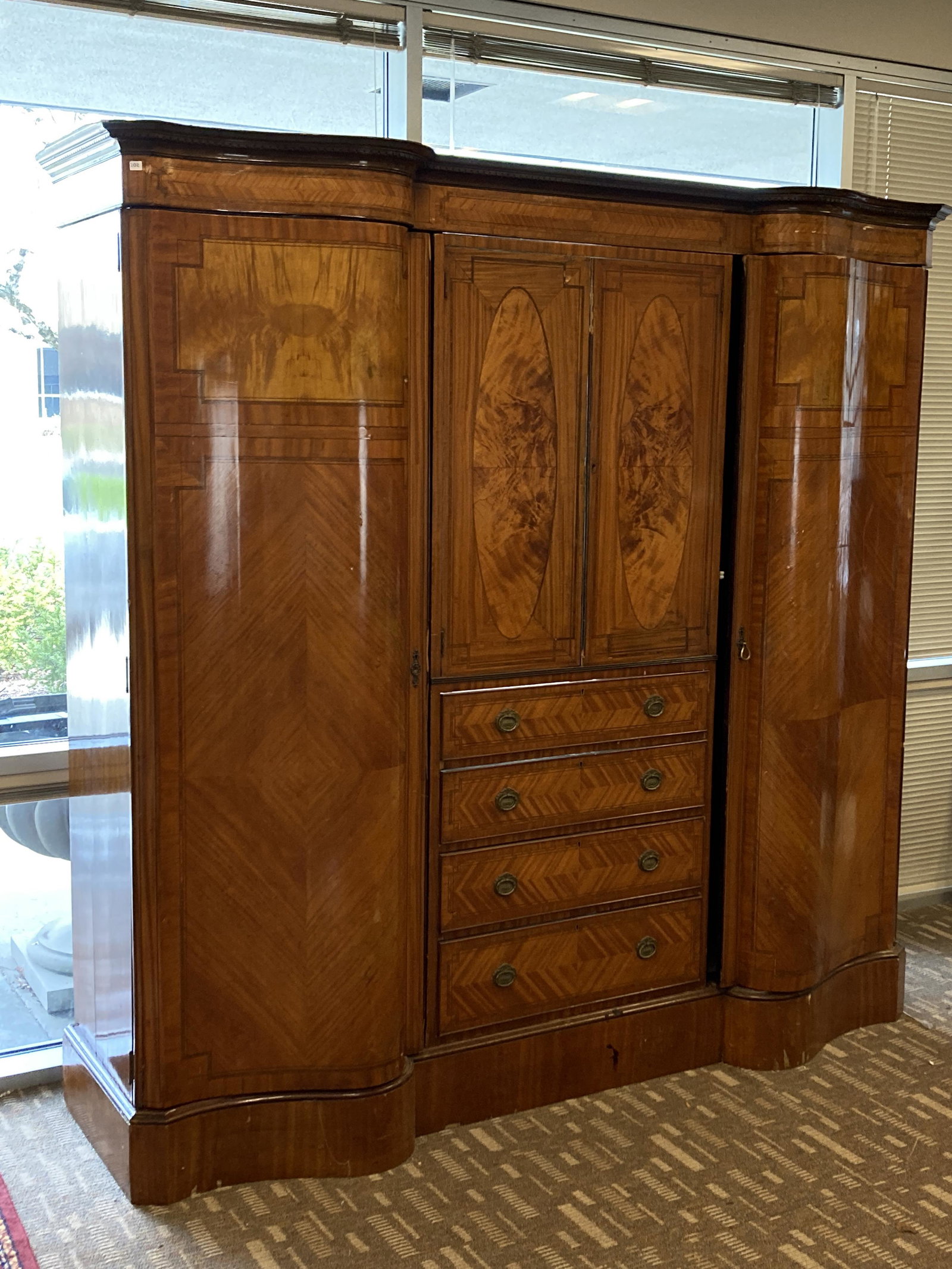European Edwardian Serpentine Triple-Door Wardrobe: An unusual Edwardian European serpentine triple-door wardrobe with decorative veneered panels in ovals and bookmatched string and other border inlays it consists of two-full length doors on either sid