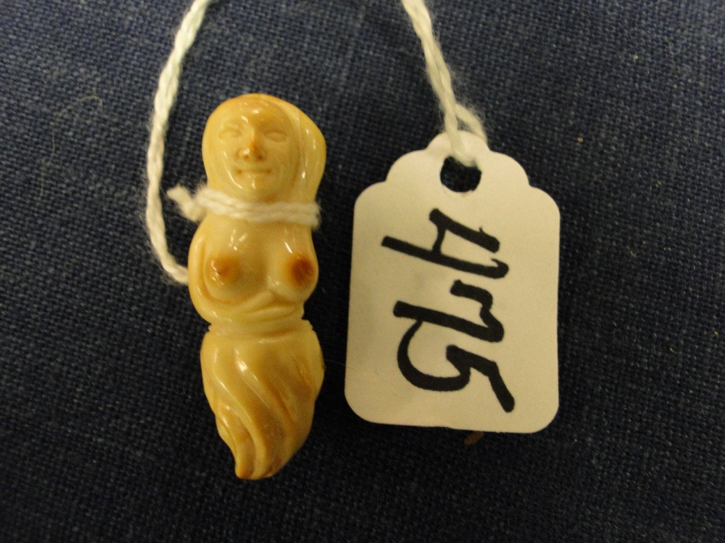 Petrified Mammoth tusk carved into the figure of a: Petrified Mammoth tusk carved into the figure of a topless woman. 1-1/4" high. Est. value $60-80.