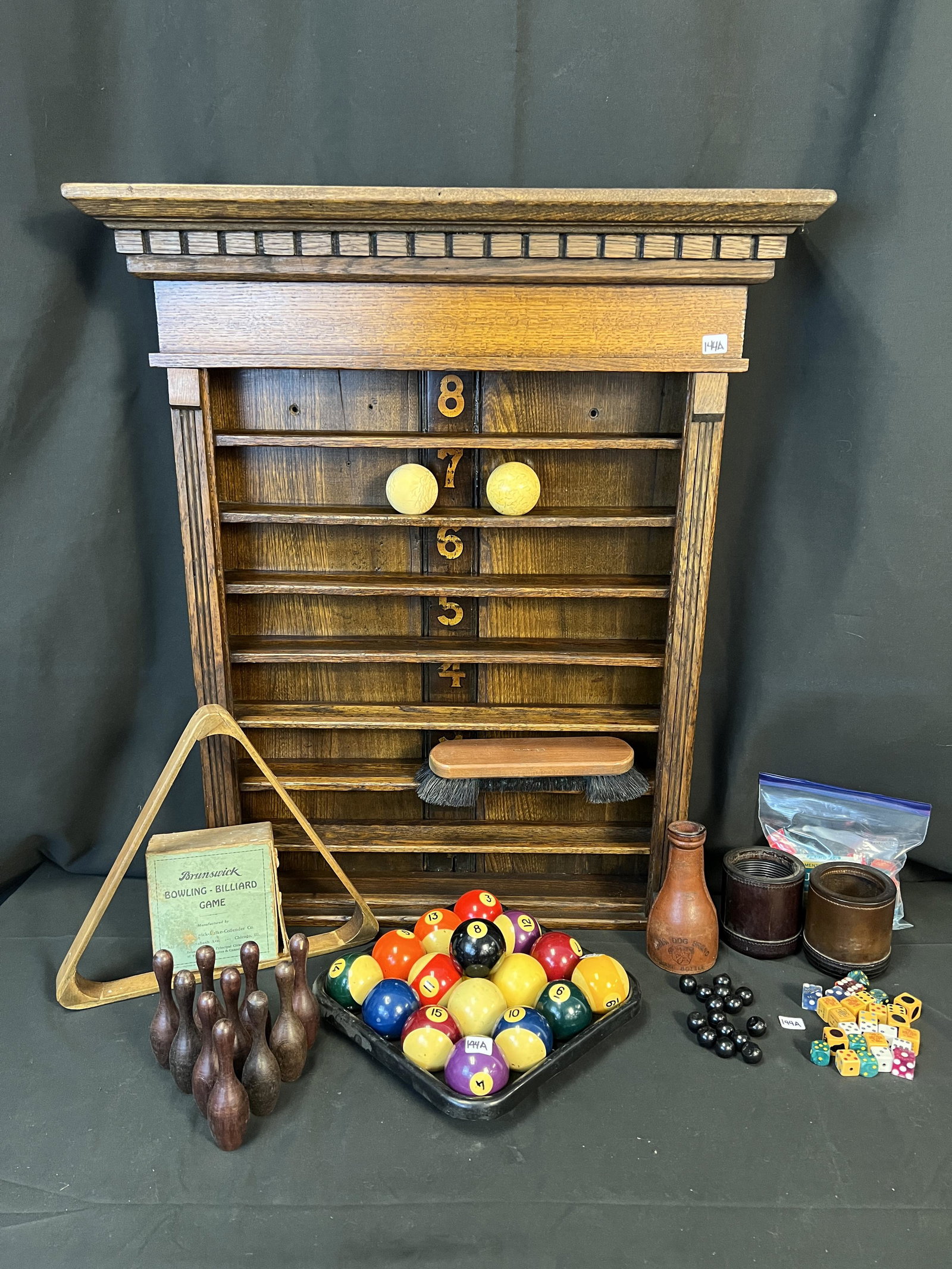 Brunswick-Balke-Collender Ball Rack & Other Billiards Accessories: A Tiger Oak Wall-Hung ball rack with original stencilied numbers and dental tooth crown in original finish along with a complete set of billiard balls, 2 ivory cue balls from the 1880s, a ball brush, 