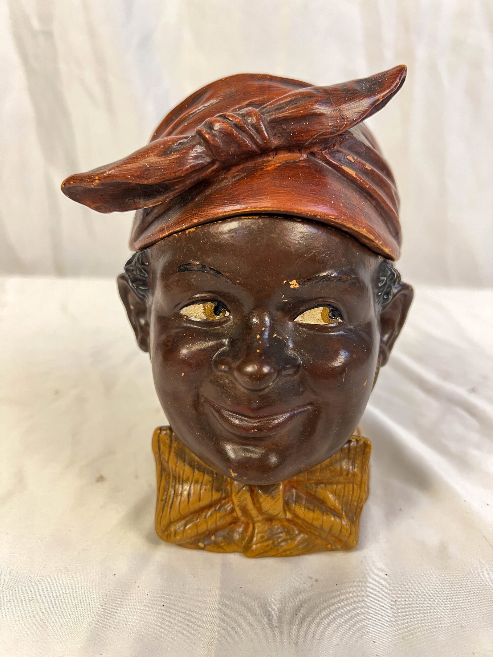 A terracota humidor of a black man's head: A terrocota humidor of a black man with dew rag hat and fancy bow tie in good condition. It measures 7"Tx7"W