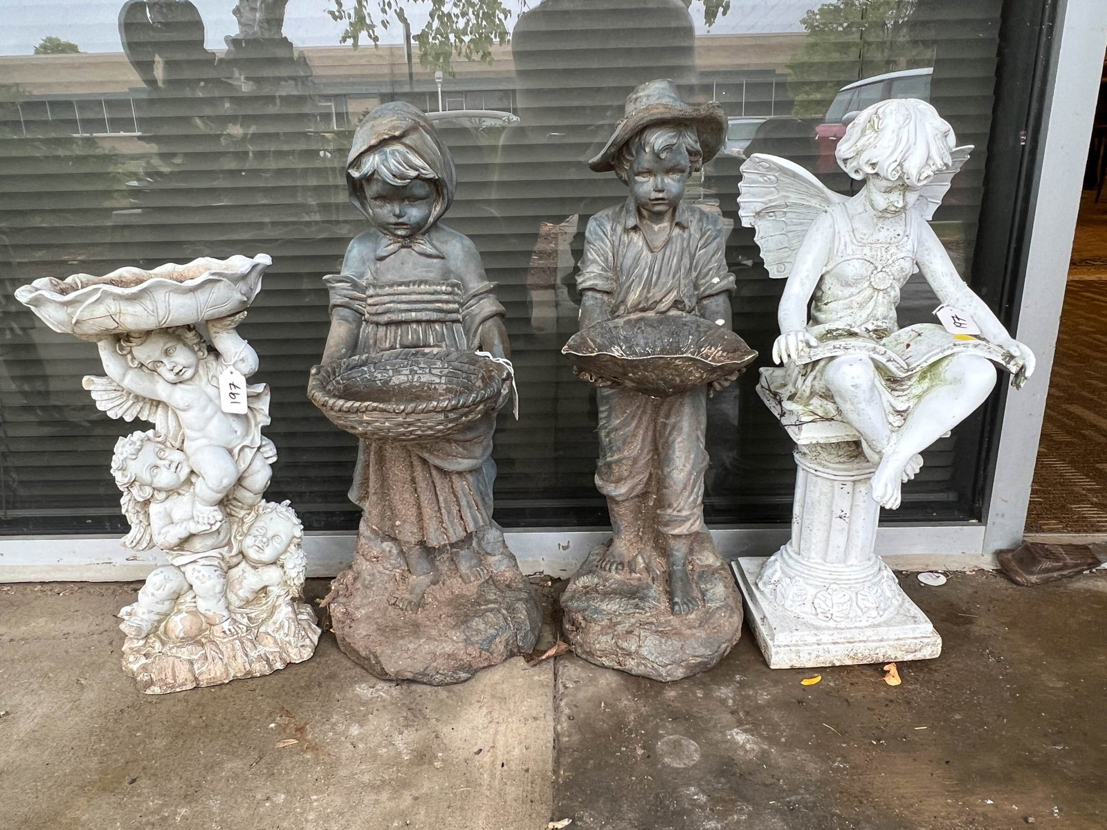 Group of four yard statues.: A group of 4 molded yard statutes. One of a fairy, one of a cupid. one of a boy and girl. The fairy measures 20in tall by 9in wide. The cupid measures 16i tall by 8 1/2 in wide. The boy and girl measu