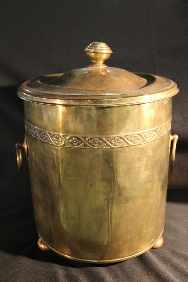 Covered brass ash holder. 2 handles. Impressed flo: Covered brass ash holder. 2 handles. Impressed floral trim near top. Sets on 3 round copper feet. Measures 12" high by 11" round. Dents.