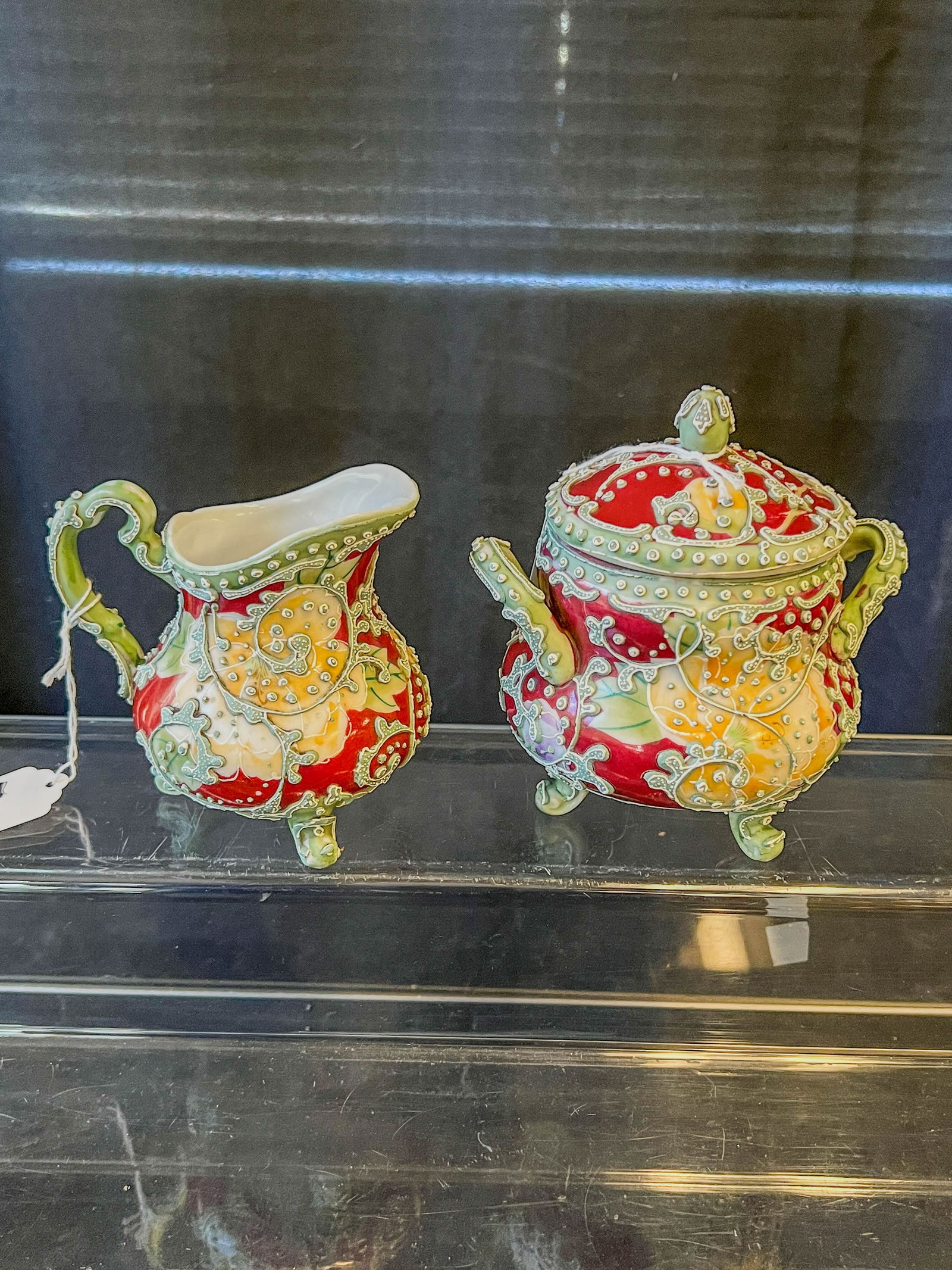 Moriaga Nippon Creamer and Sugar: A Moriaga unsigned Nippon creamer and sugar in burgundy and blue with heavily raised decorations depicting a phoenix. Covered sugar measures 5.25" tall X 5.5 across, creamer is 4" tall X 4" across.