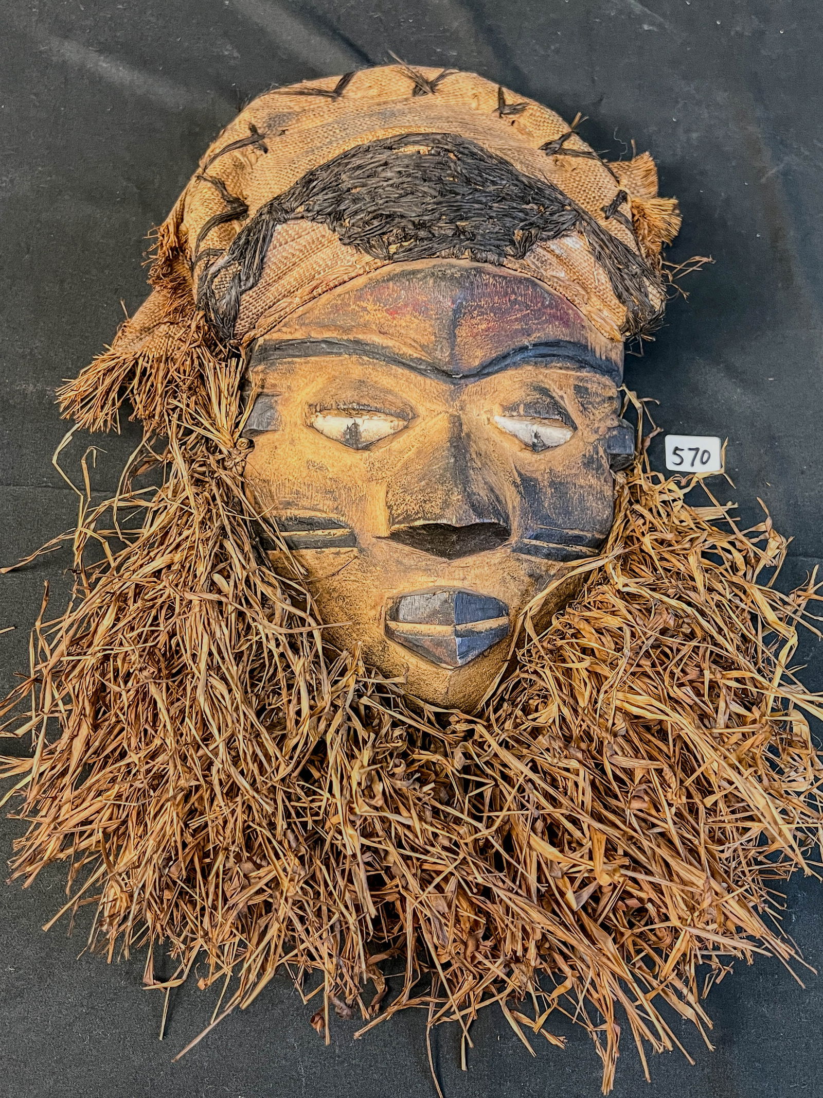 African Antique Pende Ceremonial Mask-Masculine: This antique African ceremonial mask is by the Pende, and is made of grasses, carved wood, and hand woven cloth. It measures 16" tall X 8" across.