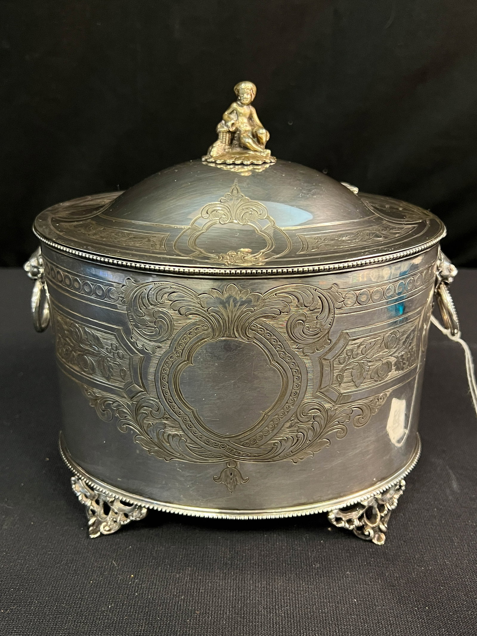 An English Silver Plate Tea Box 1800s: English silver plate footed tea box with putto finial with elaborate chasing and lion head handles. This wonderful English silver plate tea box has touch marks on the bottom and is in great condition.