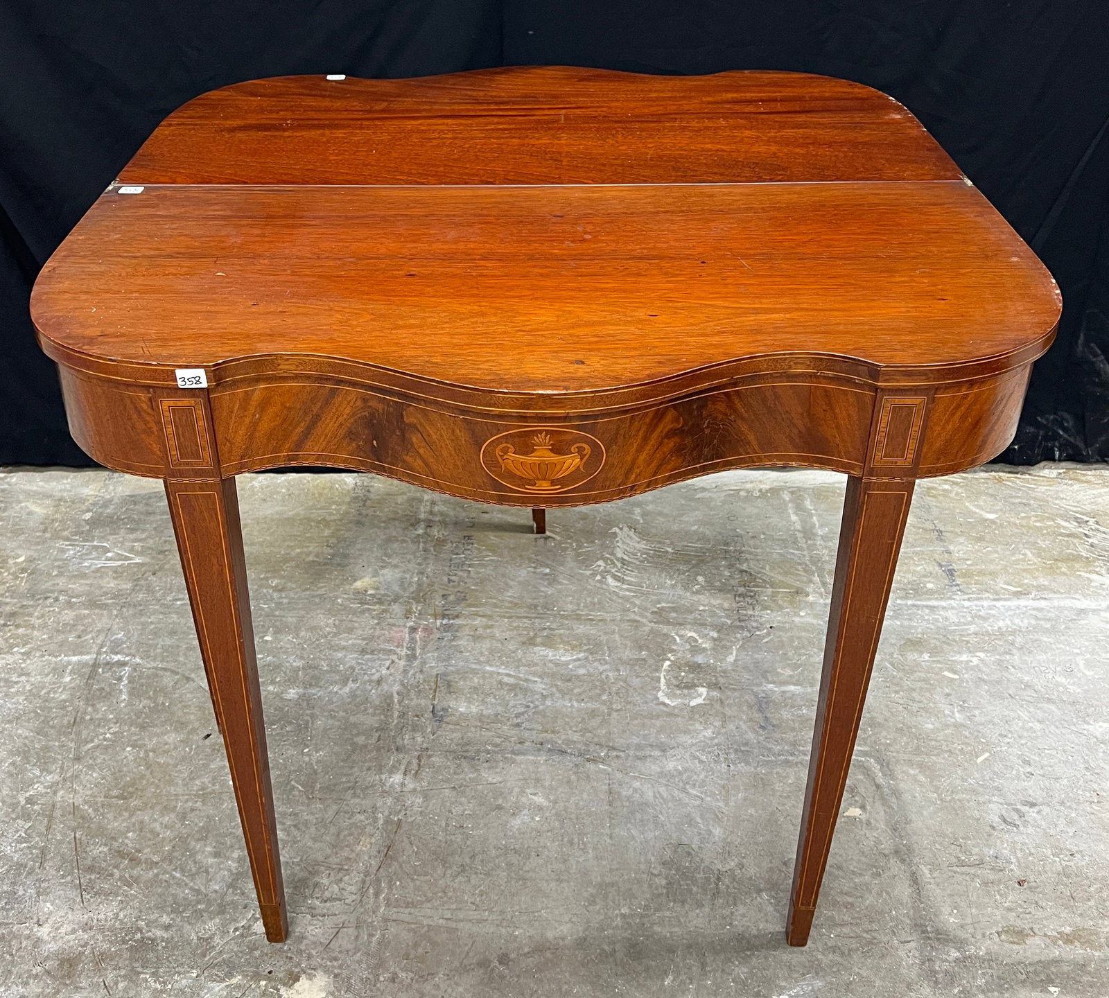 A Federal Style Serpentine Front Entry/Game Table: A Federal style serpentine front entry/game flamed mahogany table from 1900-1920. It has string and urn inlays, pencil legs, and it is in excellent original finish. It measures 29" x 35" x 33"