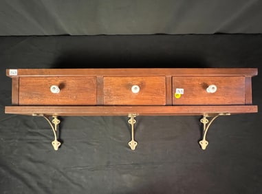 A Wall Mounted Three Drawer Dovetail Shelf With Brass Brackets