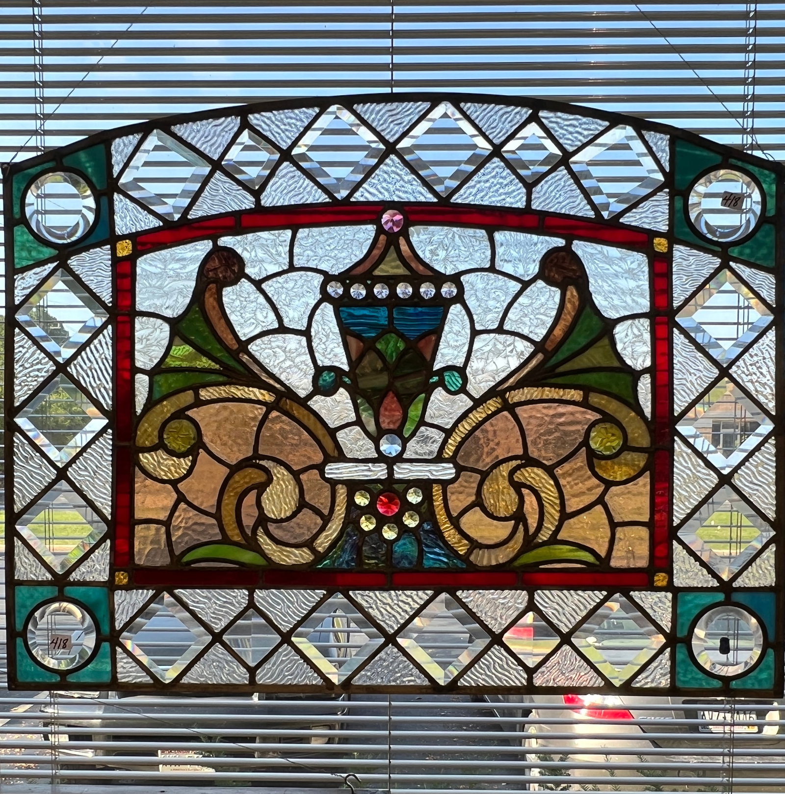 An Antique Victorian Fancy Leaded Glass and Stained Window: An antique Victorian arched top stained and beveled glass window with elaborate jeweled urn and fancy multicolored cornucopias with a ruby border. This wonderful window is out of an Old World Milwauke