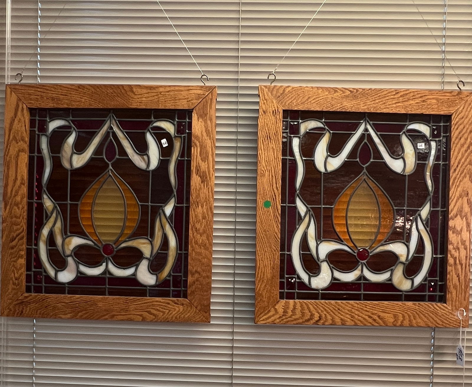 An Antique Pair of Art Nouveau Stained Glass Windows: An antique pair of Art Nouveau stained and leaded glass windows in a ribbon pattern with jewels and a ruby background. They are in new oak frames. The windows themselves are antique but newly framed.