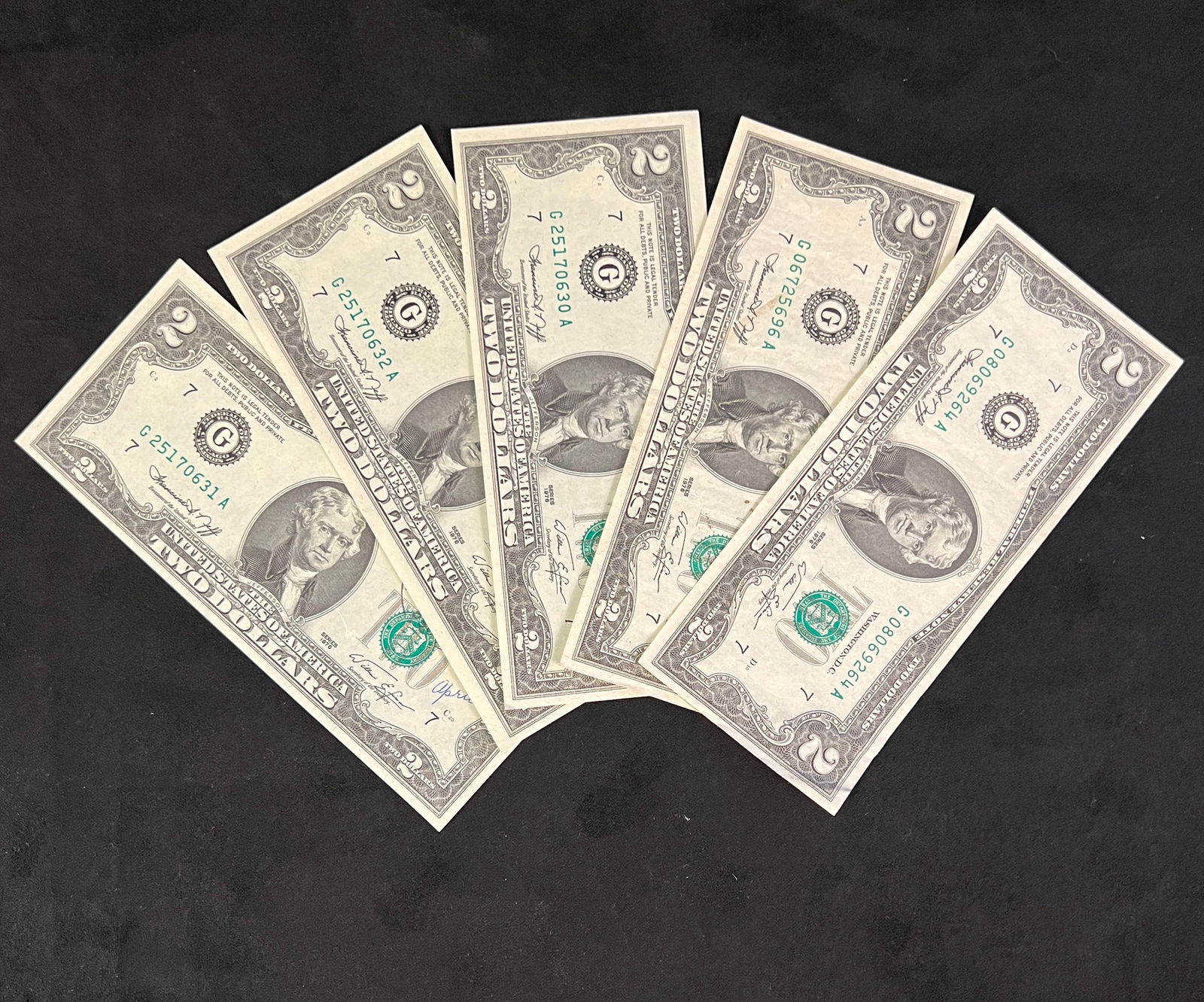 Five Two dollar Bills Series 1976`: Five two dollar bills. Three of the bills are uncirculated. Two of which have "Thiensville APR 13 1976 PM 53092" stamped with postmark stamps applied. The third uncirculated has the same postmark stam