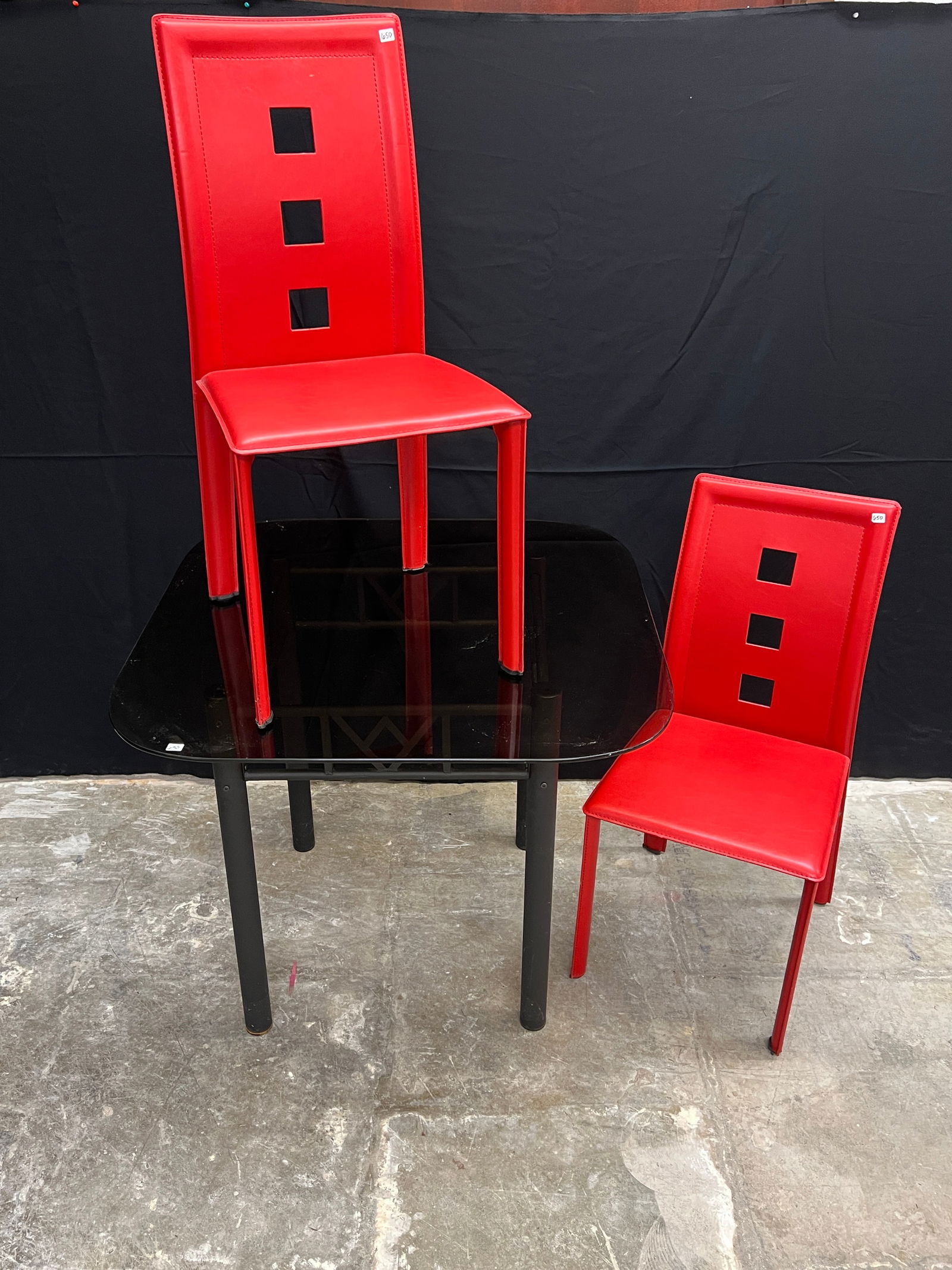 2 Post Modern Red Chairs and Glass Top Table: A small Post Modern Dinette Set to include a square smoked glass top table with black metal base and 2 red high back chairs with square cutouts in excellent condition. table measures 30" tall X 35.5"
