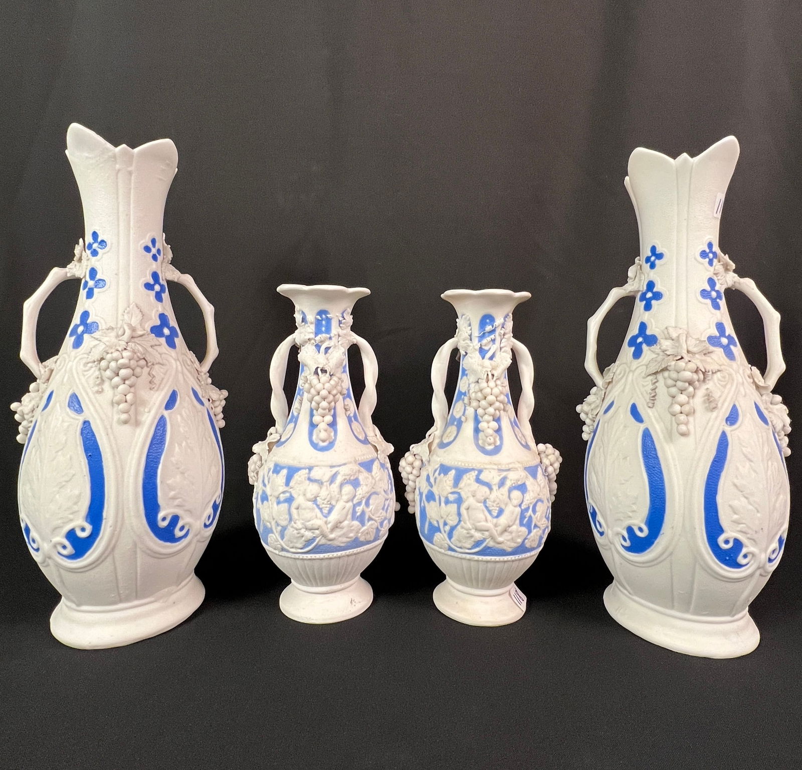 Group of Parian Ware Vase, c1830-70: A group of four antique Parian ware vases, two large and two small. These unglazed porcelain vases in blues and white feature intricate, high-relief designs including grape clusters, leaves and