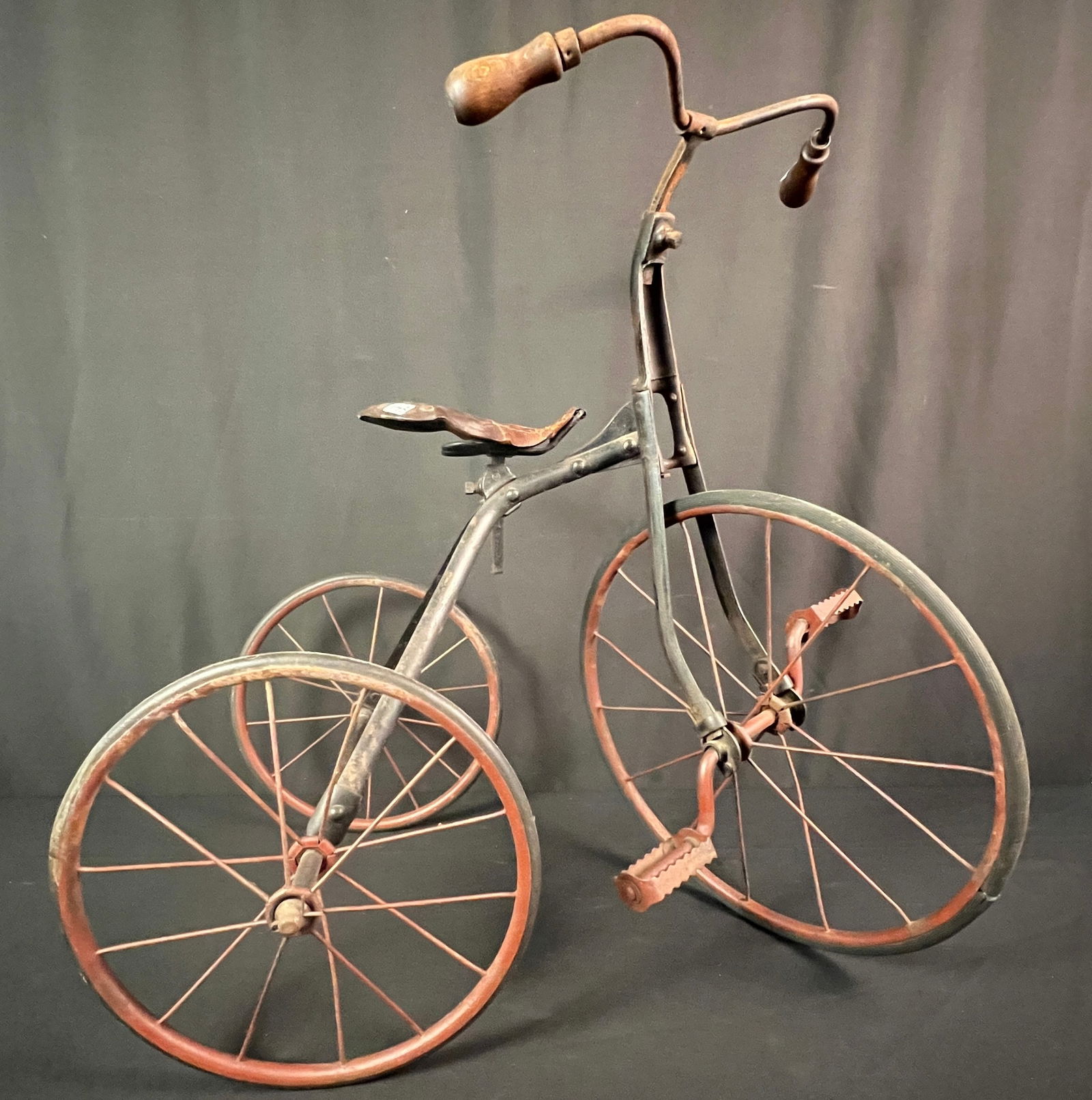 Turn of the Century Iron Tricycle c1900: An antique turn of the century child's tricycle that features a leather riveted seat, original red paint on wheels, and original rubber on wheels. In good, as found condition this measures