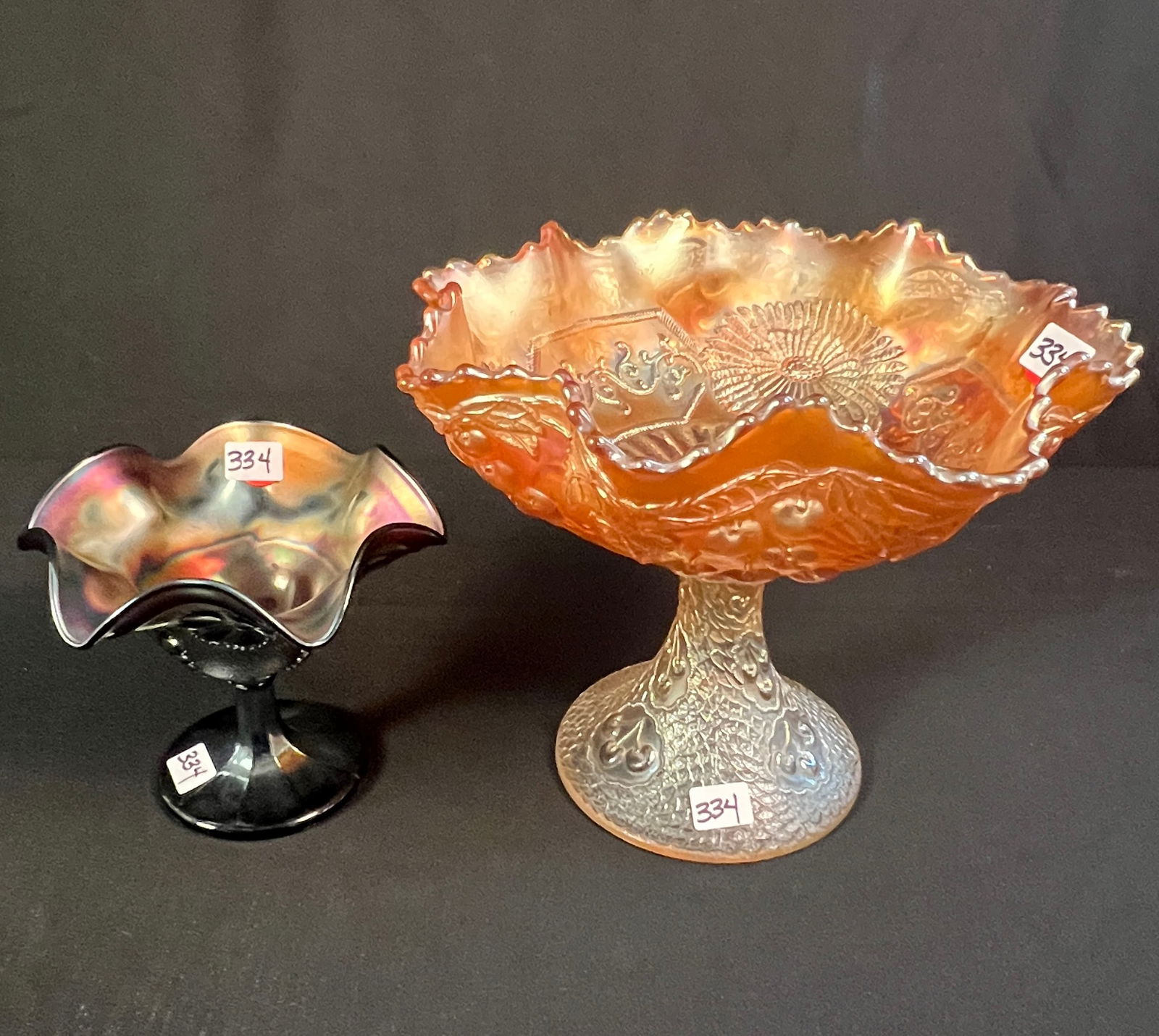 Oversized Carnival Glass Compote and One Other: An oversized Marigold carnival glass compote with cherry blossom exterior and mums interior, measuring 8" tall X 10" across. Along with an amethyst carnival glass small compote, measuring 5.5" tall X