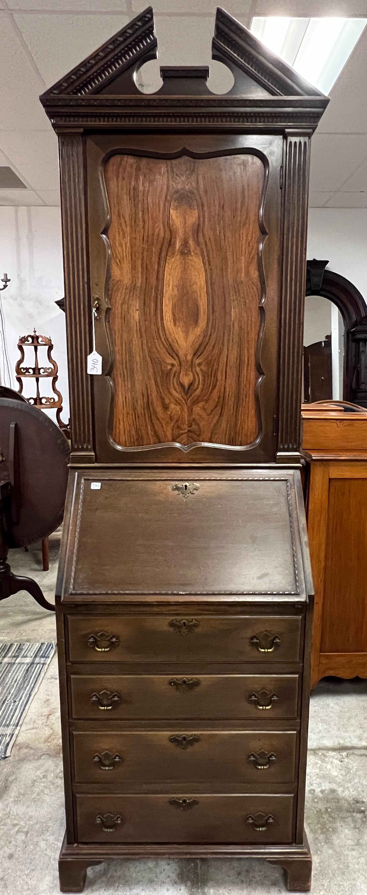 Chippendale Petite Secretary: A 1920s Chippendale mahogany drop front secretary with single door, flamed mahogany bookcase top, book matched rosewood center panel. This petite secretary has a fancy arched pediment, pillared front