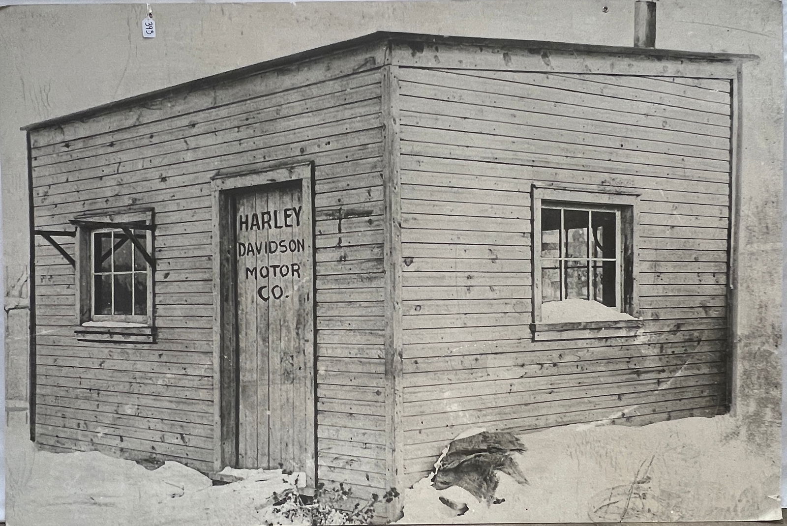 Harley-Davidson Photo Reproduction of Original Factory: A large reproduction of a historical photograph of the original Harley-Davidson Motor Company factory. Pictured is the small, wooden shed built in 1903 in the Davidson family's backyard, with "Harley