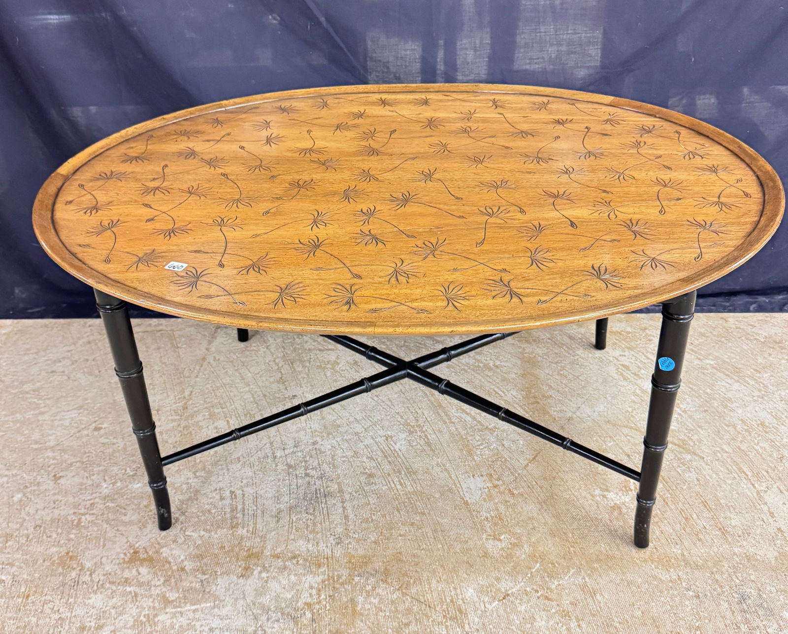 Kittenger Oval Cocktail Table: An oval mahogany coffee table by Kittenger, with the Kittenger label on the underside that features a raised lip, inciesd dandelion seed pattern on the top and ebonized faux bamboo carved legs and str