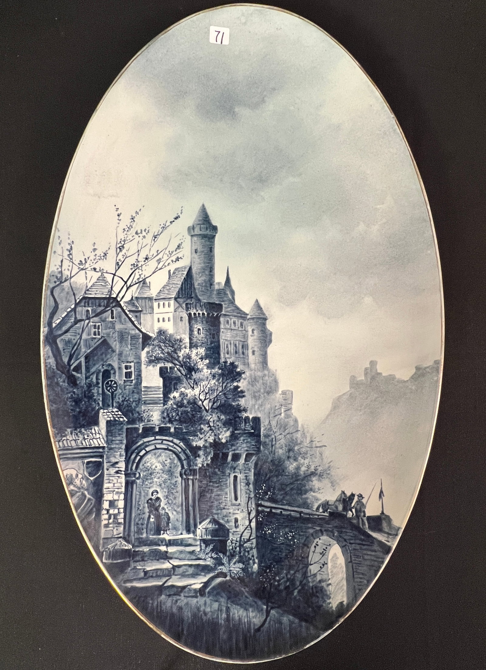 19th Century Oval Hand Painted Wall Charger: A porcelain hand painted oval wall charger c.19th century depicting an elaborate castle, maiden and child in a mountainous woodland landscape. In blue tones with a gold rim, it is signed on the back