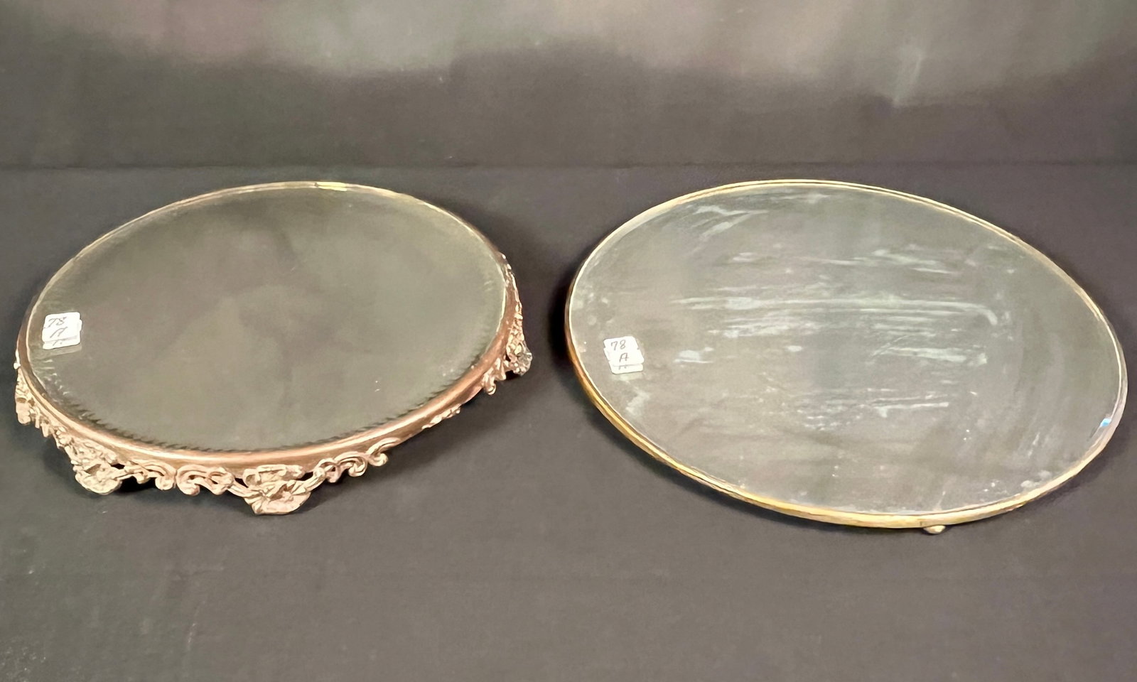 Two Beveled Mirrored Plateaus: Two beveled mirrored plateaus, one with zipper cut and floral edging (12" round) and the other is on small ball feet (13" round). In excellent, house ready condition.