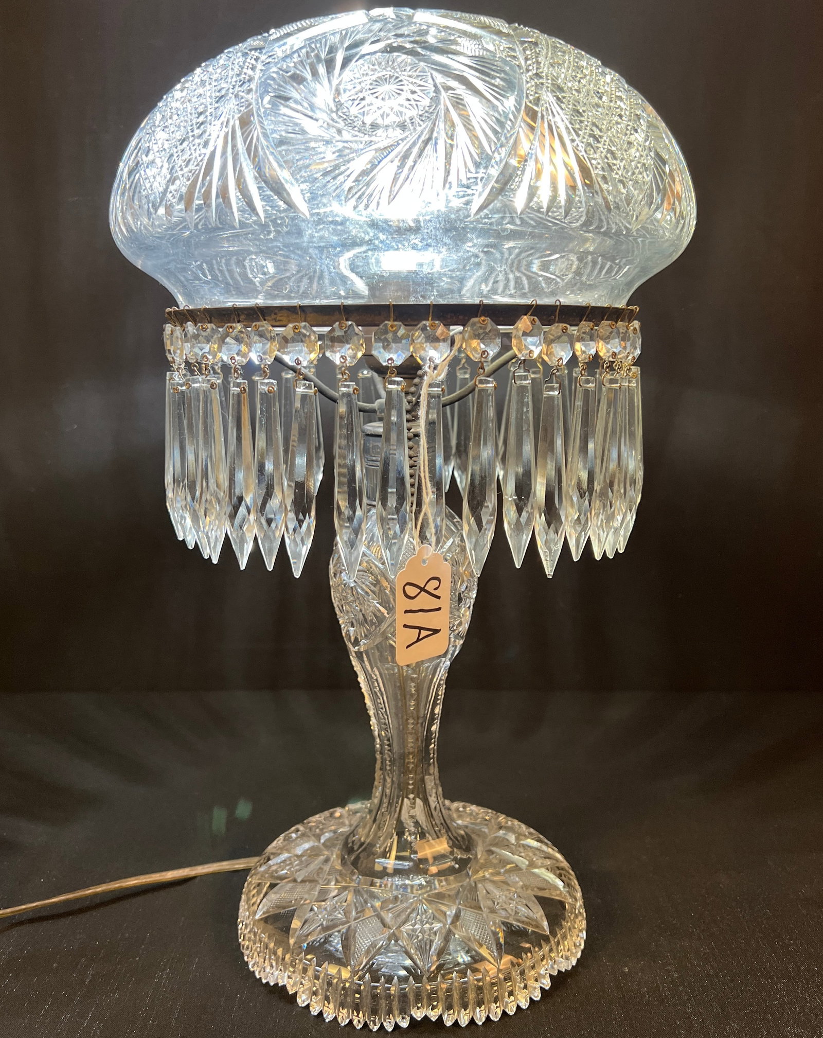 Turn of the Century Cut Crystal Lamp: A turn of the century cut crystal lamp with domed crystal shade. This elaborate zipper and pinwheel cut table lamp is in excellent condition. The base is wheel and diamond cut, and it is trimmed in