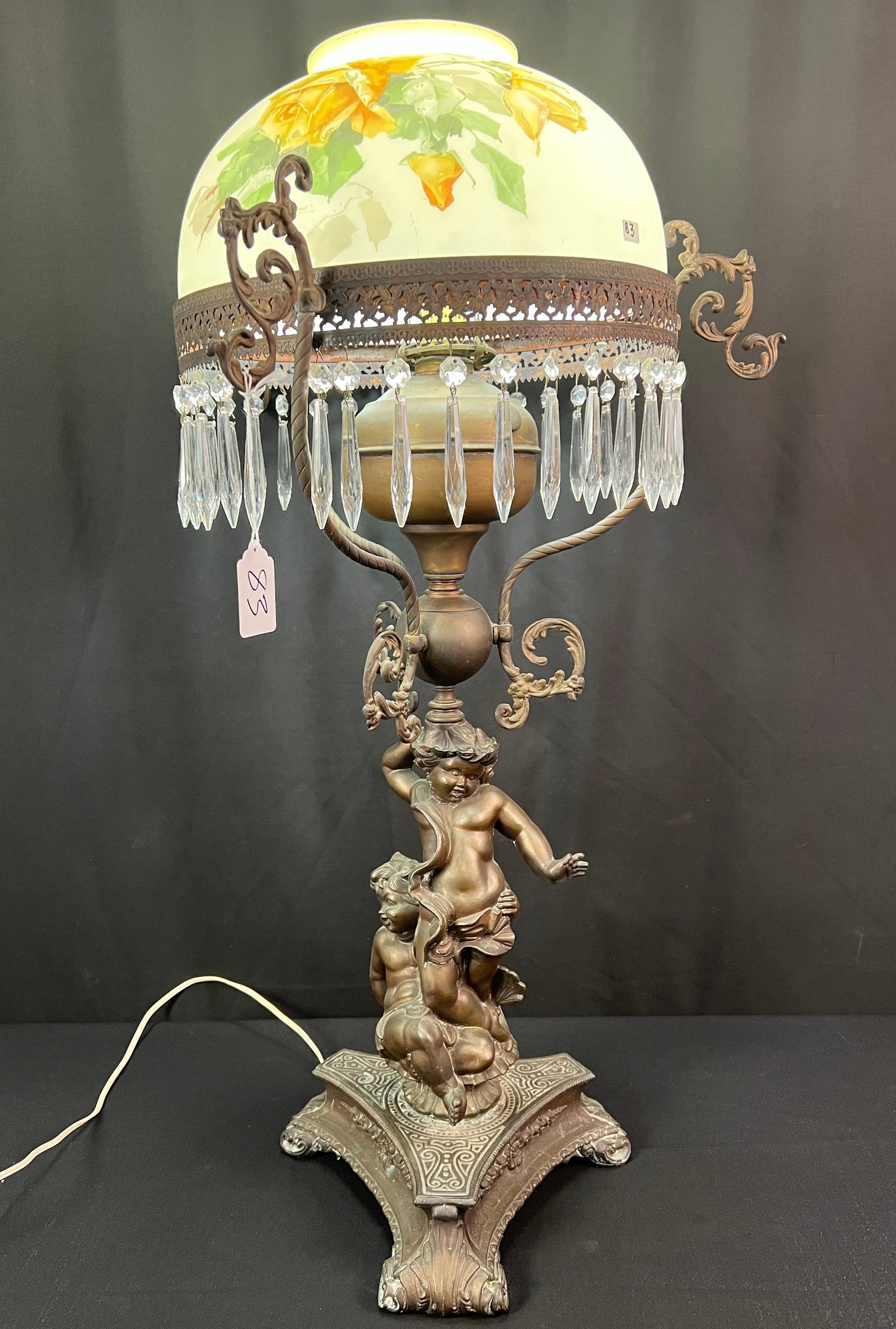 Electrified Brass Figural Cupid Oil Lamp with Hand painted Shade C 1890's: A fancy brass electrified figural oil lamp c.1890's that features a hand painted rose shade, crystal prisms, and a base with two cupids. In measures 36" tall X 18" across.