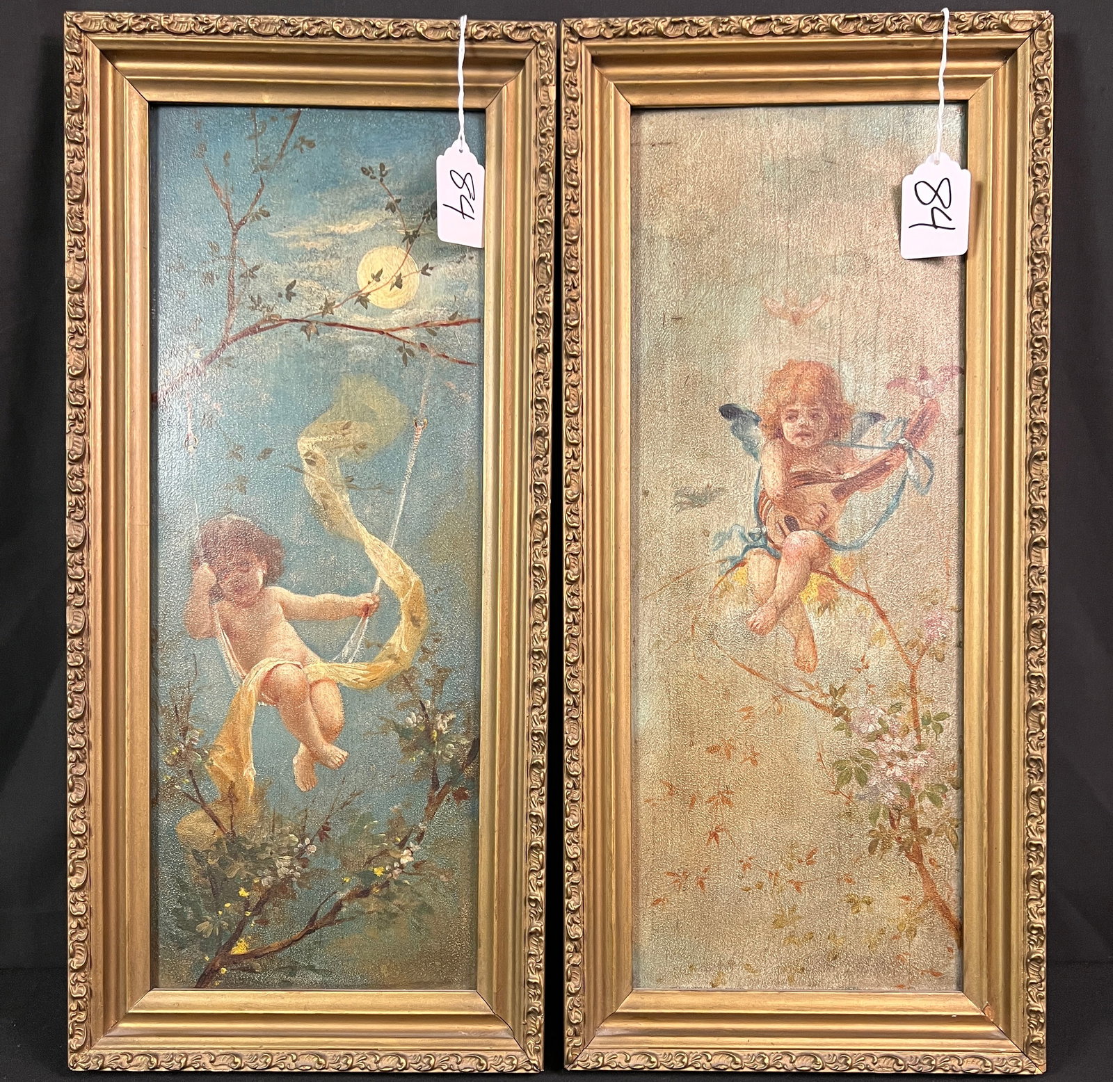 Victorian Pair of Oils on Board Cupid Paintings C 1890's: A pair of quality period framed Cupid/Puti, unsigned c1890's. One painting depicts a cupid playing a lute sitting in the branches of apple tree, and the other is a night scene of a puti swinging