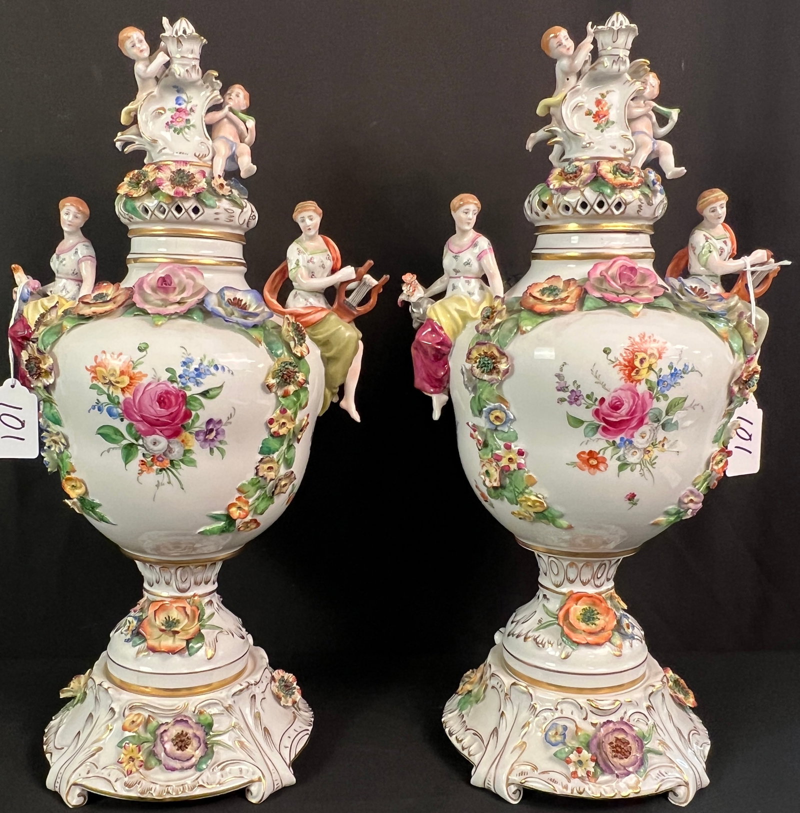 Pair of Von Scheirholz lidded Porcelain Urns c1907-1930's: A large pair of matching German porcelain lidded mantle urns by Von Scheirholz c.1907-1930'sthat feature figural handles, puti, and flowers. Several flowers missing petals but in good overall conditio