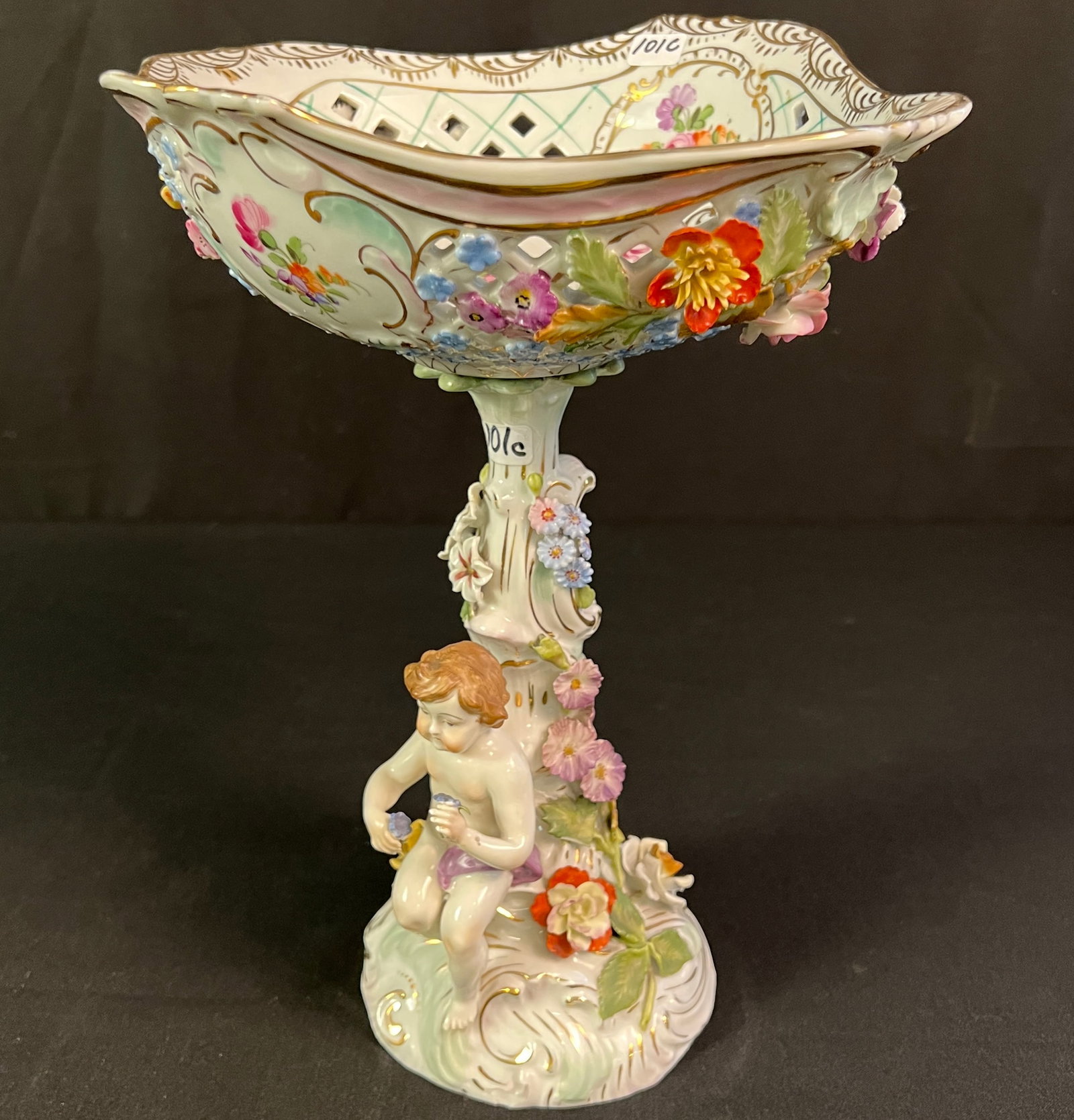 Carl Thieme Porcelain Footed Compote: A hand painted, pierced and garland decorated footed compote with reticulated bowl over a stem adorned with a full figural puti and three dimensional flowers by Carl Thieme, Dresden. In very good cond