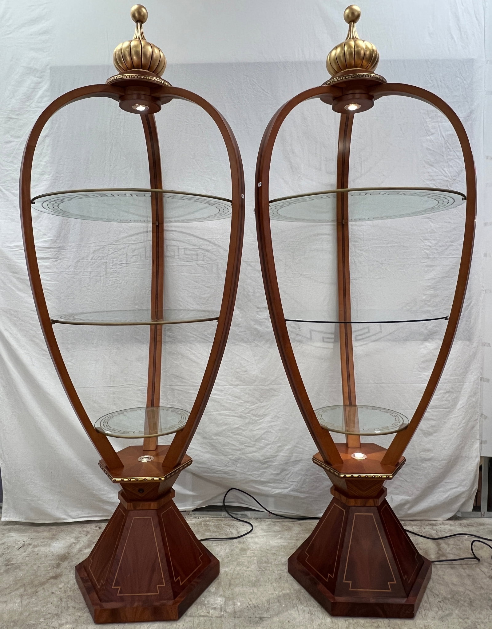 Two Carpanelli Lighted Mahagony Etageres: Two Carpanelli contemporary mahogany lighted etageres that feature three graduated glass shelves, string inlay, and large gold crown finials. They measure 88" tall by 32" across. The middle shelf on