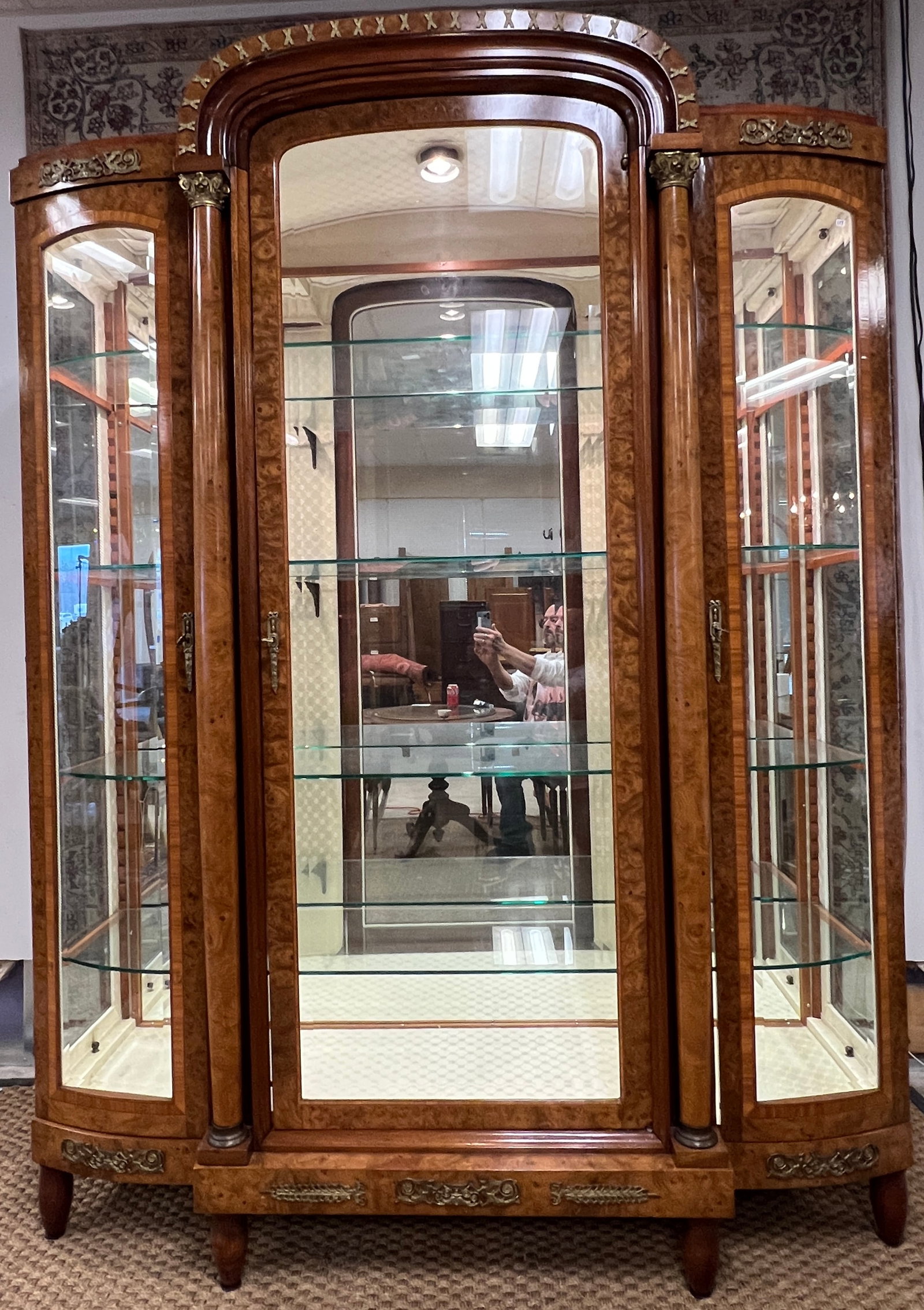 French Style Burled Mahogany Glass front Display Case: A deluxe late 20th Century ornate French style light up display case that features fancy ormolu, burled mahogany, string inlay, beveled glass central door and sidelights, glass shelves, Corinthian col