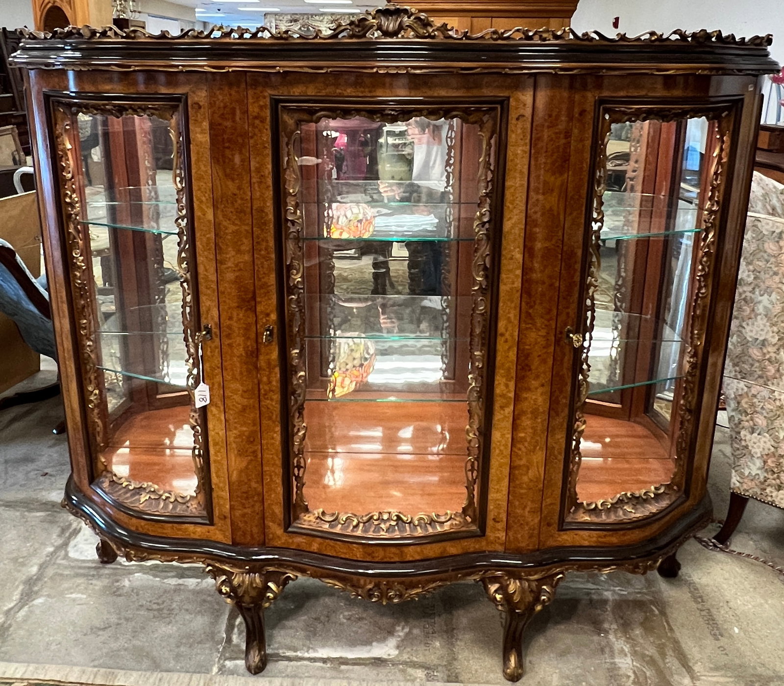 Italian Floral Carved China Cabinet: A stunning late 20th century profusely carved Italian style illuminated China cabinet that features pierce carved gallery and carved edging, carved cabriole legs, burled mahogany finish, mirrored