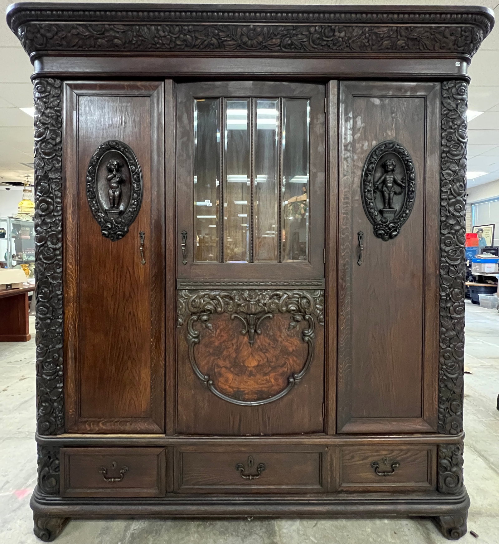 Victorian Floral Carved Oak Armoire c.1880's: A Victorian Floral carved Oak armoire that features 3 lower drawers, heavy carved crown and corners, 4 leaded glass beveled panels above a burled central carving, Puti Carved medallions on each side