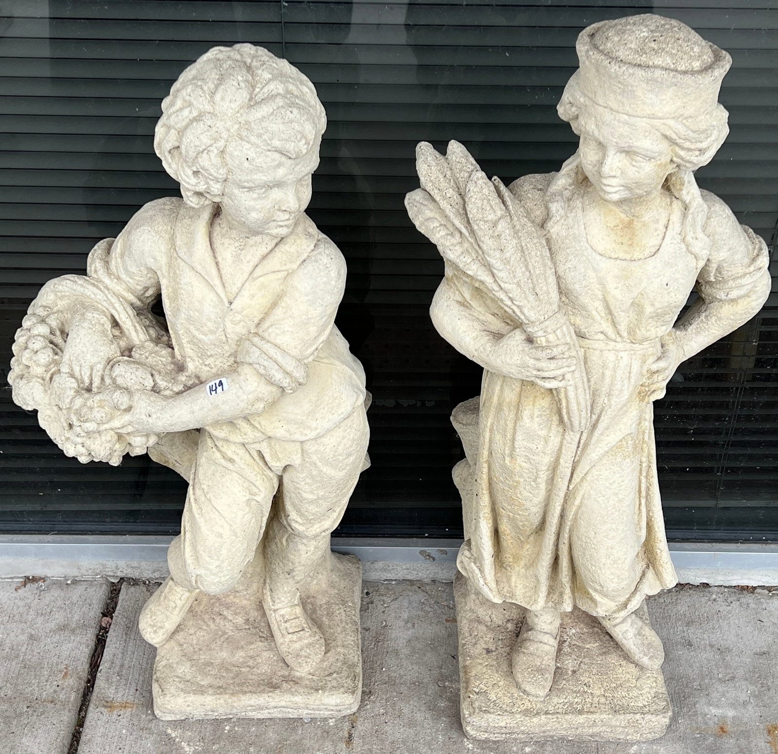 Pair of Antique Concrete Garden Figures: A pair of antique concrete garden figures of a girl holding wheat and boy holding a basket of fruit. In excellent condition, they approximately measures 31" tall X 14" across X 10" deep.