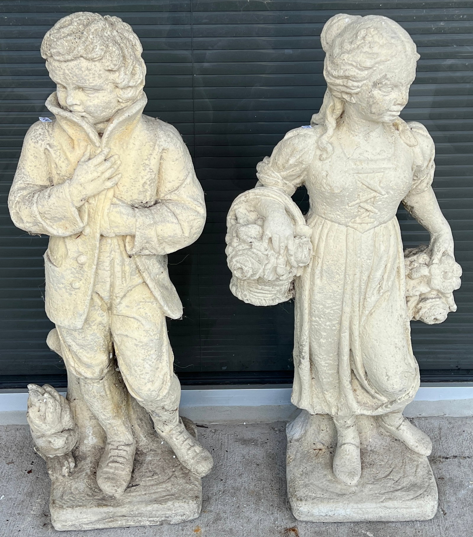 Antique Concrete Garden Statues, Pair: A pair of antique concrete garden figures of a girl holding baskets of flowers and boy is closing his coat to the cold. In excellent condition, they approximately measures 31" tall X 14" across X 10" 