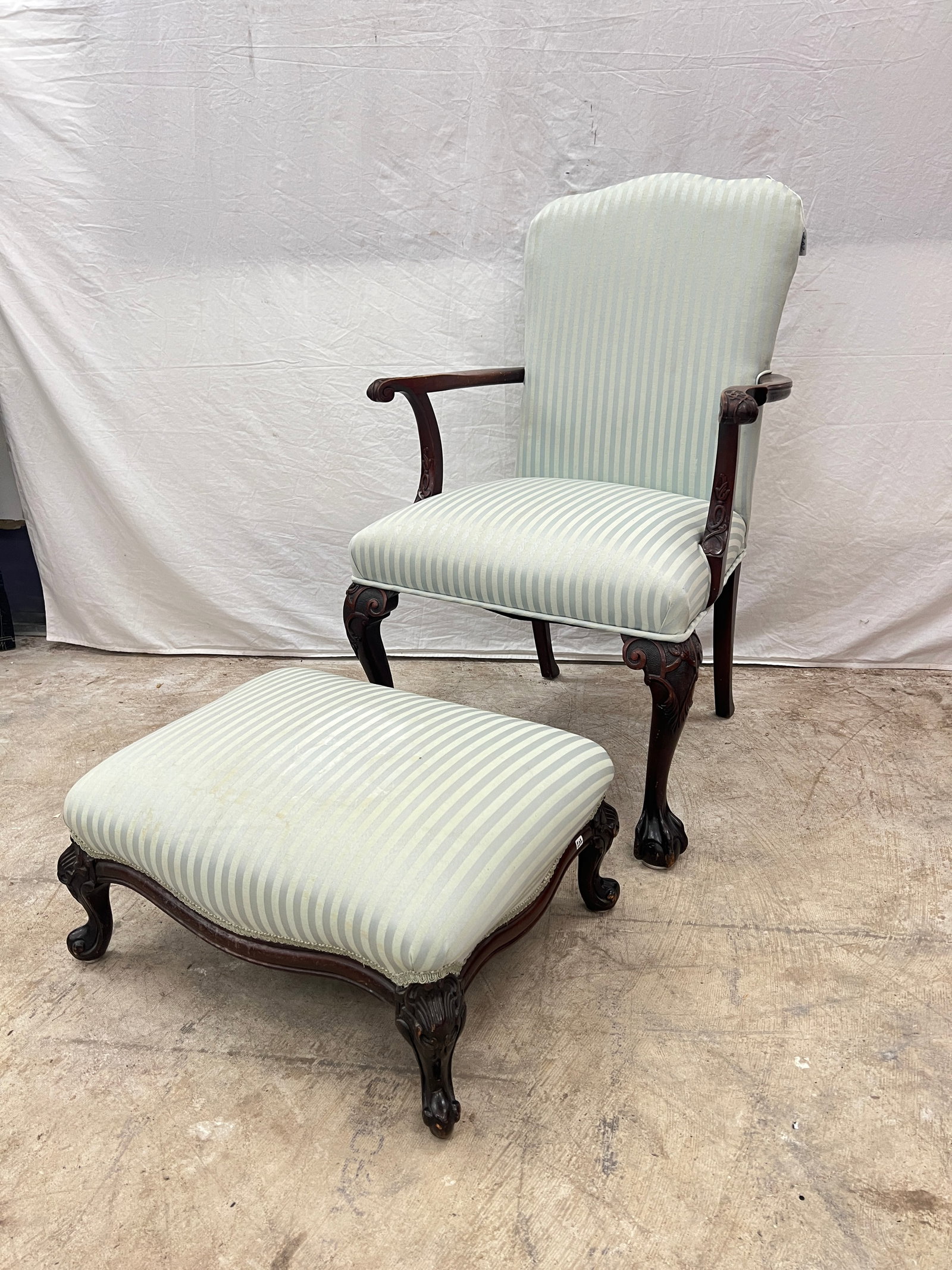 Chippendale Carved Mahogany Upholstered Armchair and Upholstered Footstool: A Chippendale carved mahogany upholstered armchair with claw and ball feet, blue striped upholstery along with a footstool in matching upholstery that measures 11" tall X 22" across X 17" deep.