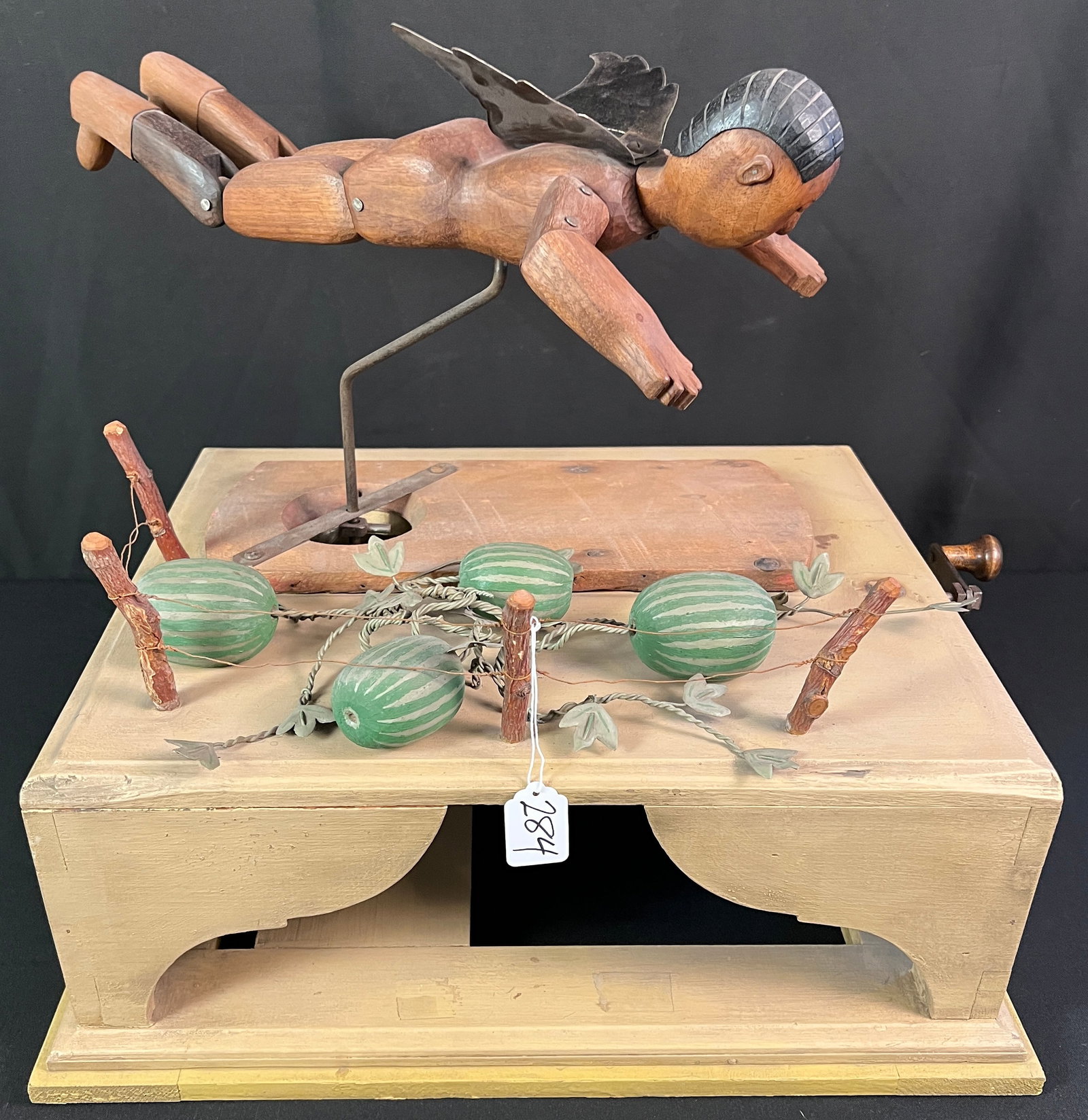 Folk Art Mechanical Angel: A Folk Art handmade mechanical angel titled "Dark Angel Guarding Watermelon Patch" . It depicts a jointed wooden angel that flies over a garden of hand painted wooden watermelon. In Excellent