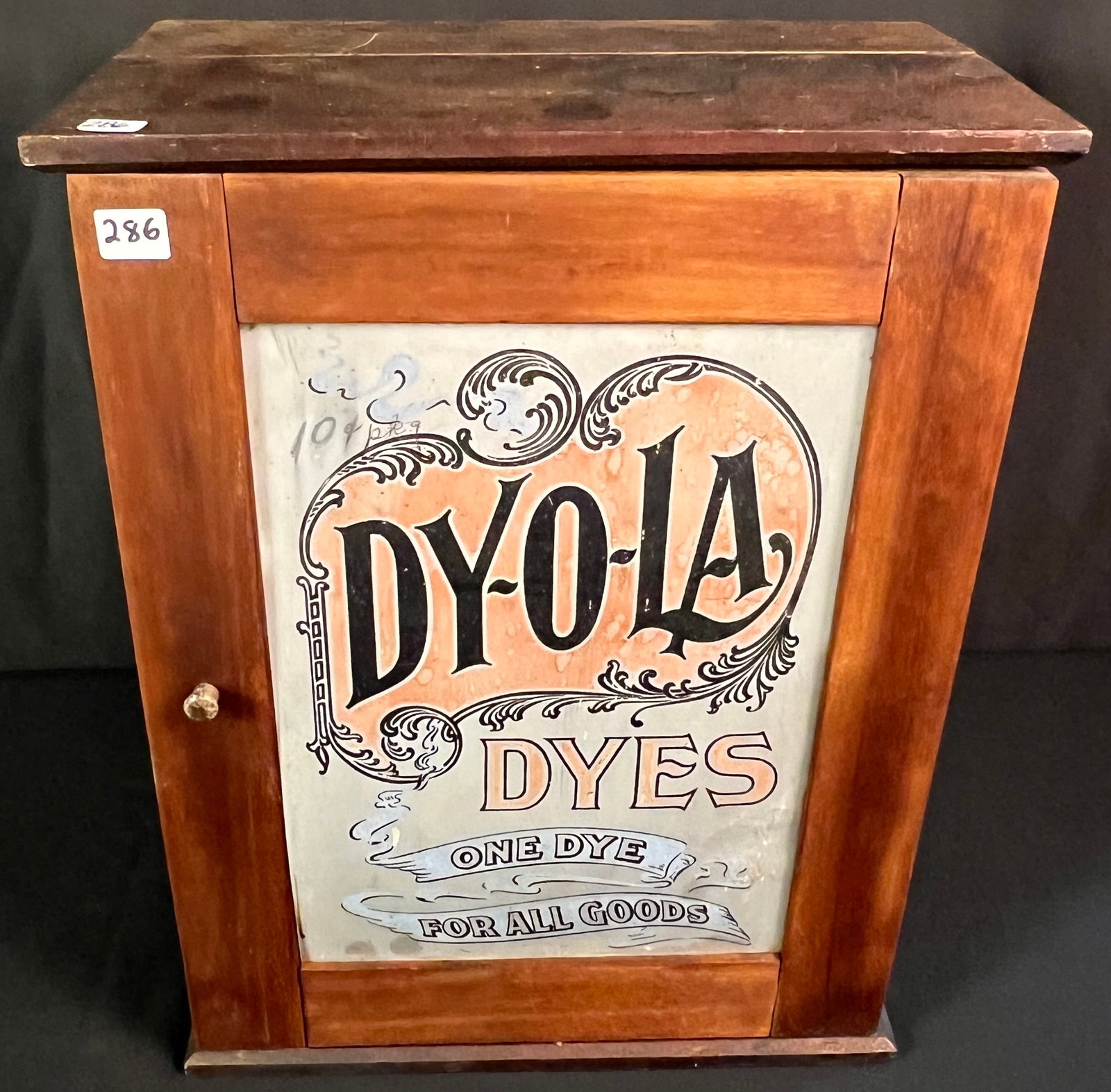Dyola Dye Box Counter Display: A Dyola Dye countertop display box with original cardboard advertising front and fitted interior where dye packets would have been kept. Cabinet has a door both on front and back. Some age wear noted