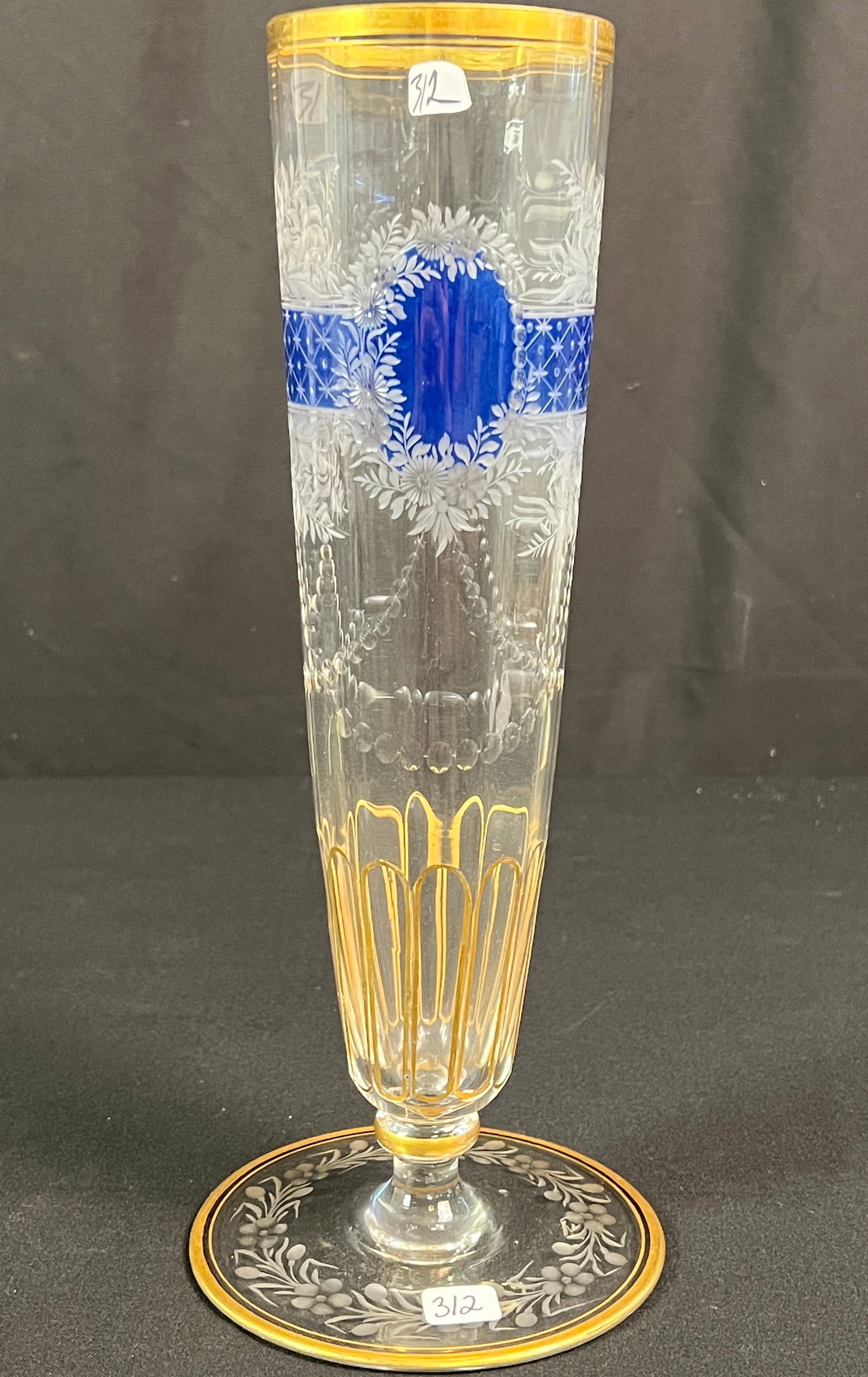 Bohemian Moser Crystal Vase: A vintage Moser Bohemian cut and etched crystal vase. It features a striking blue overlay, with intricate enamel etchings, a floral etched base, and gold gilt accents. It measures 12.5" tall X 5"