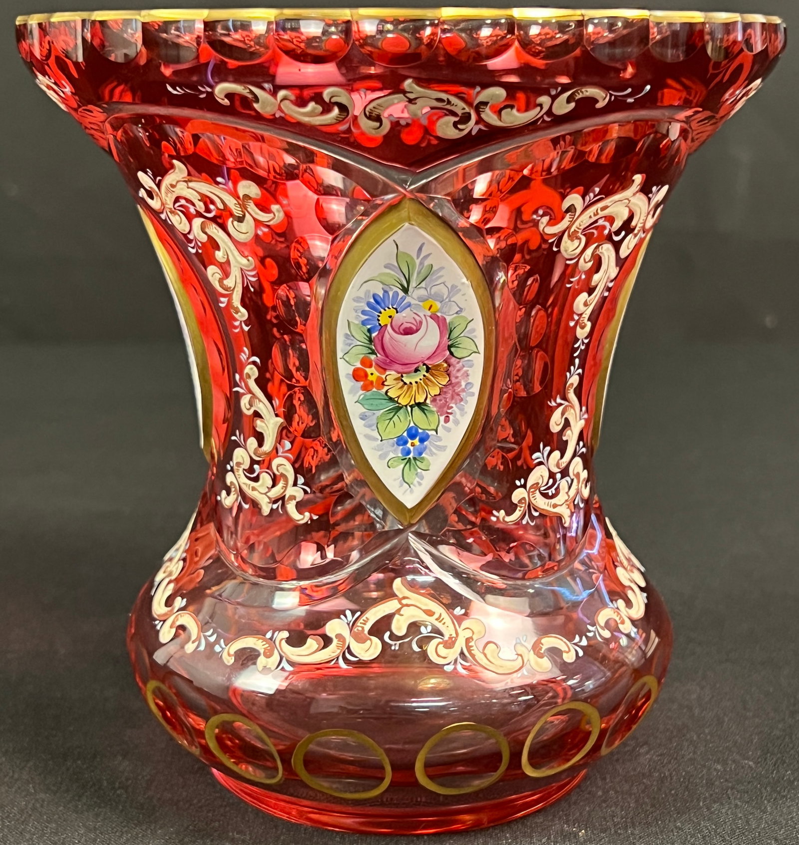 Bohemian Cranberry Glass Vase: A vintage Bohemian Czech cranberry glass crystal cut vase featuring gold gilded accents, enameled flourishes, and hand-painted floral decorations. In excellent condition, it measures 6.25" tall X 6"