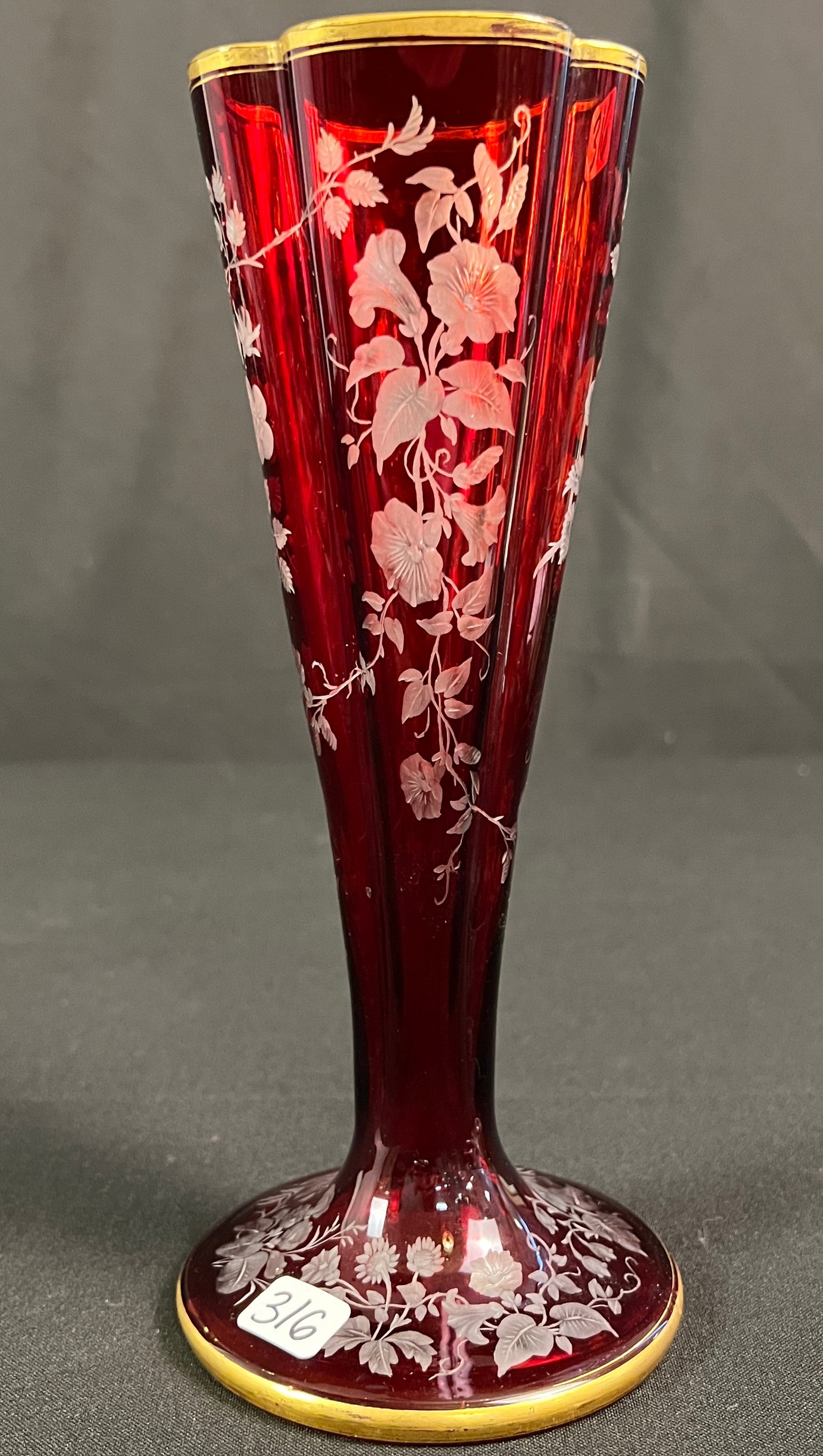 Bohemian Ruby Glass Vase: A vintage bohemian pigeon blood ruby overlay glass vase with deeply acid cut back details featuring engraved floral patterns and gold gilded edge trim. With light natural wear to the gilding, in great
