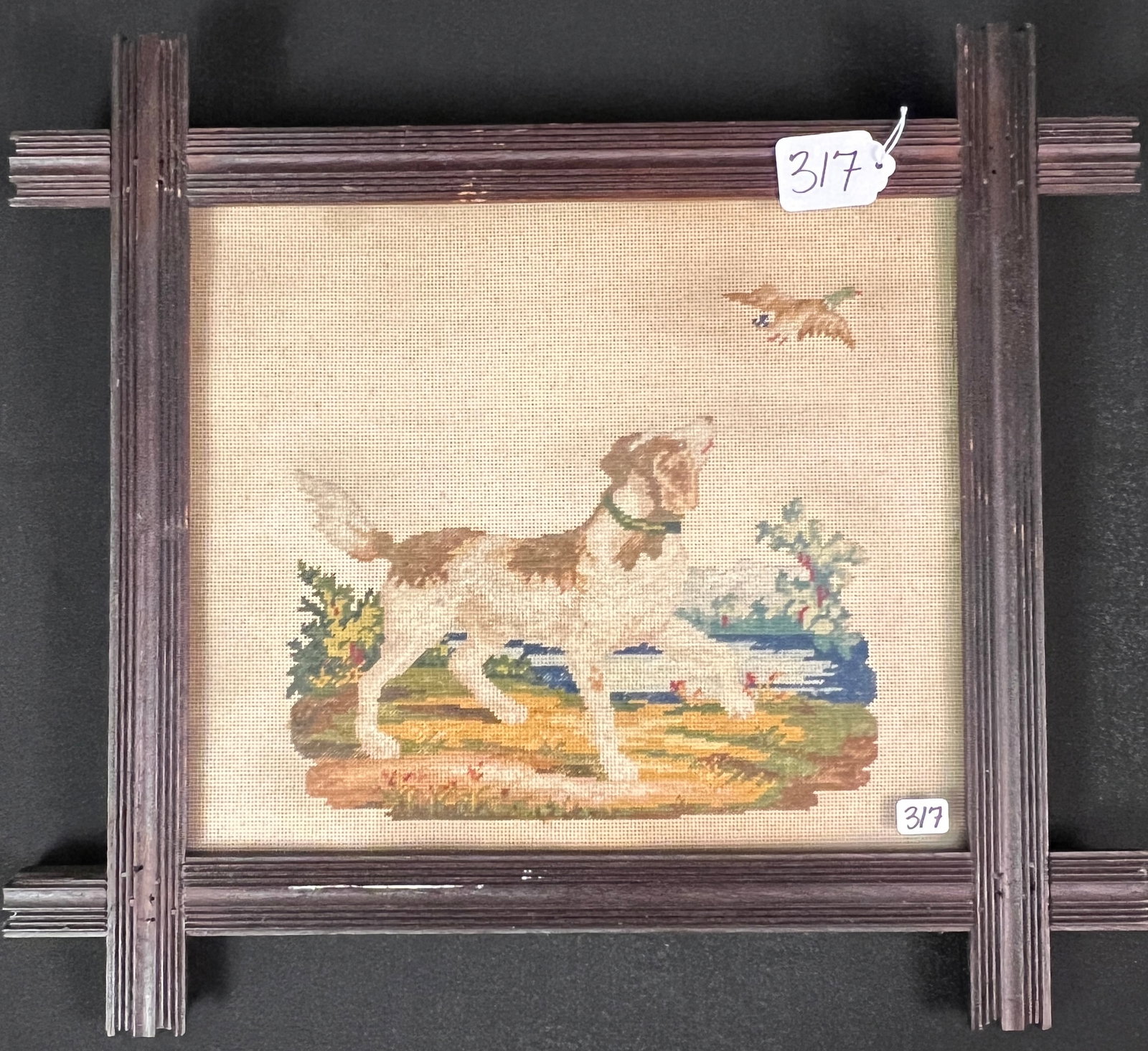 Berlin Woolwork Dog Needlepoint: A Berlin wool work needlepoint depicting a hunting dog in a rural landscape, chasing a duck. It is styled after traditional 19th century Berlin wool work patterns. In a folk art brown frame, it is in
